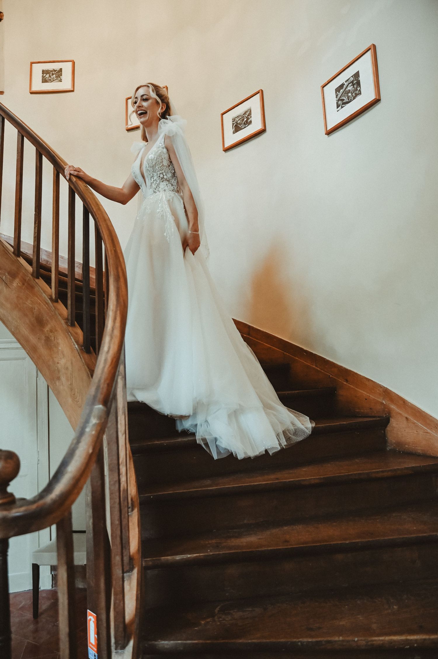 Elegant pose on a wooden staircase with white walls and framed artwork.
