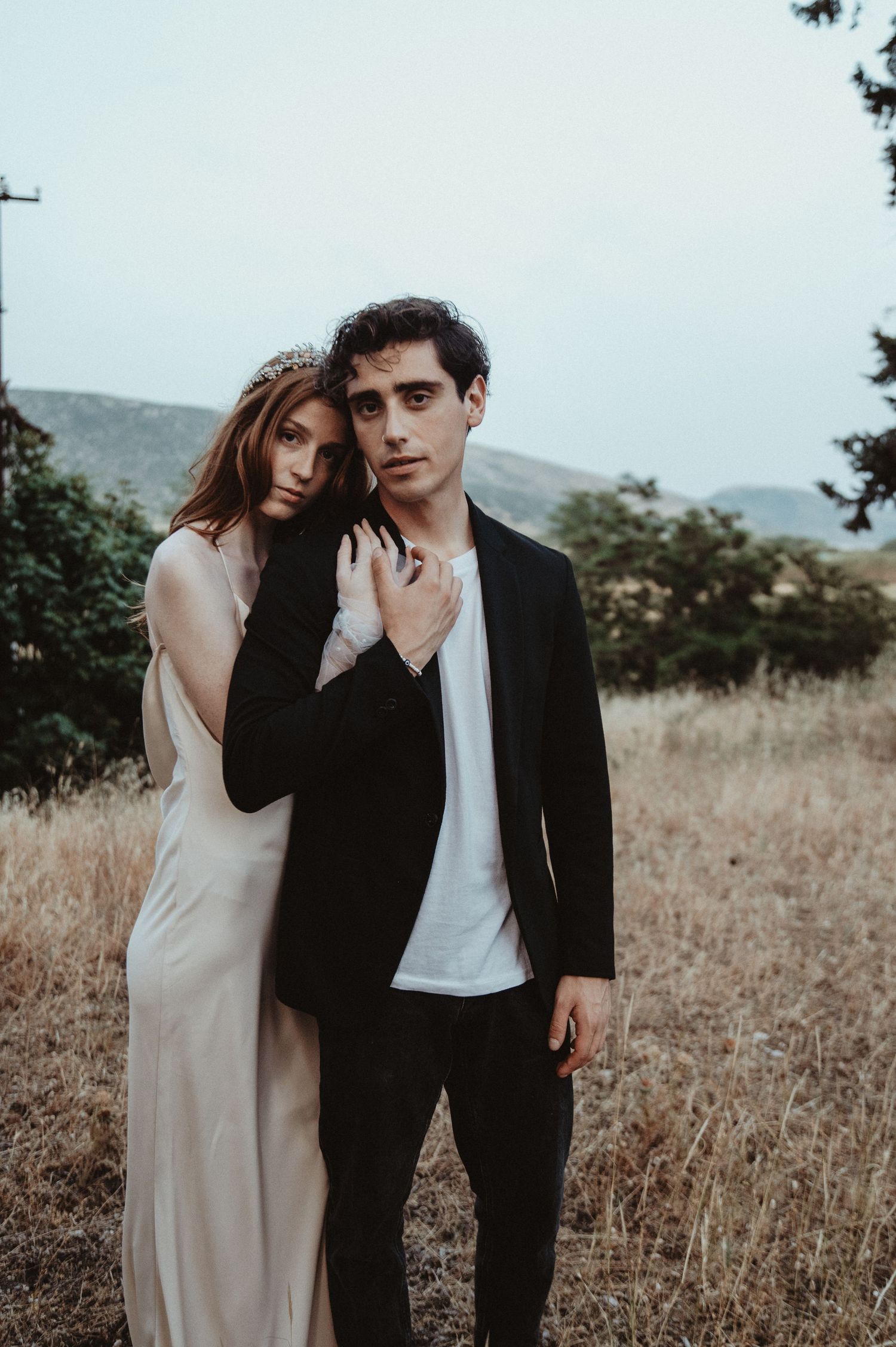 Moody outdoor portrait of newlyweds in a golden field with mountains behind.