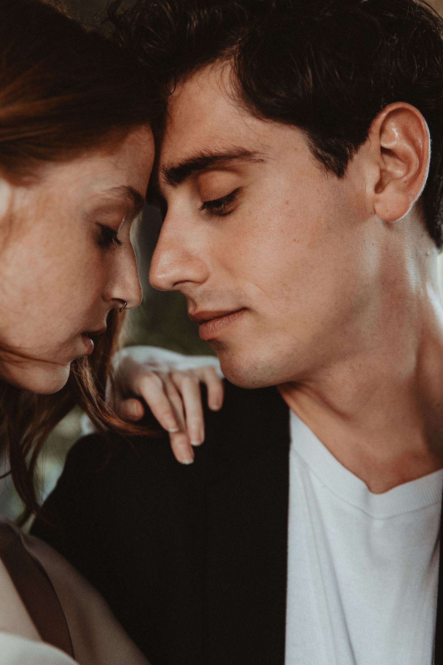 A moody intimate portrait of a couple in warm lighting with their faces close together.