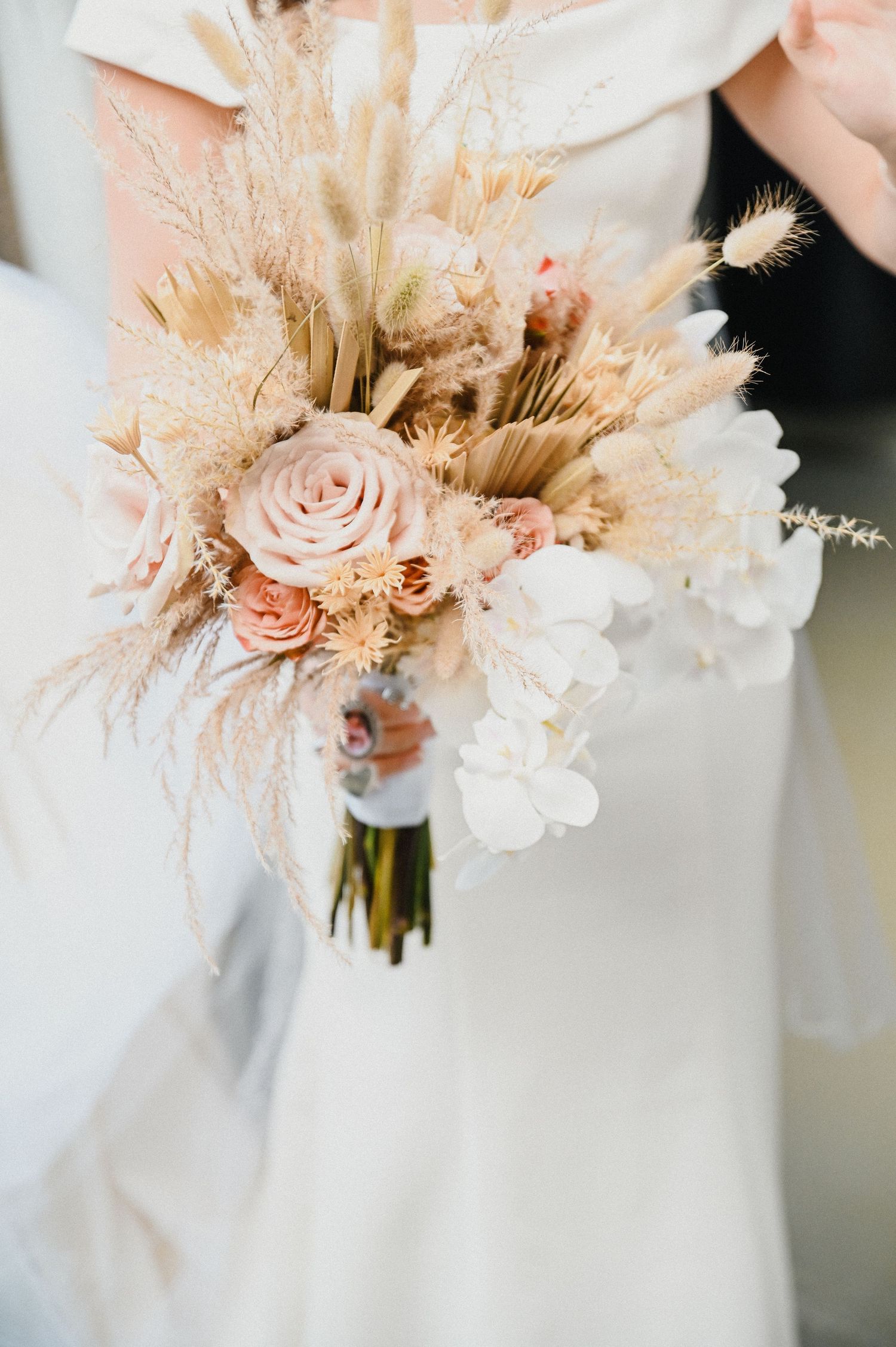Elegant bridal bouquet featuring dried pampas grass, blush roses, and white flowers.