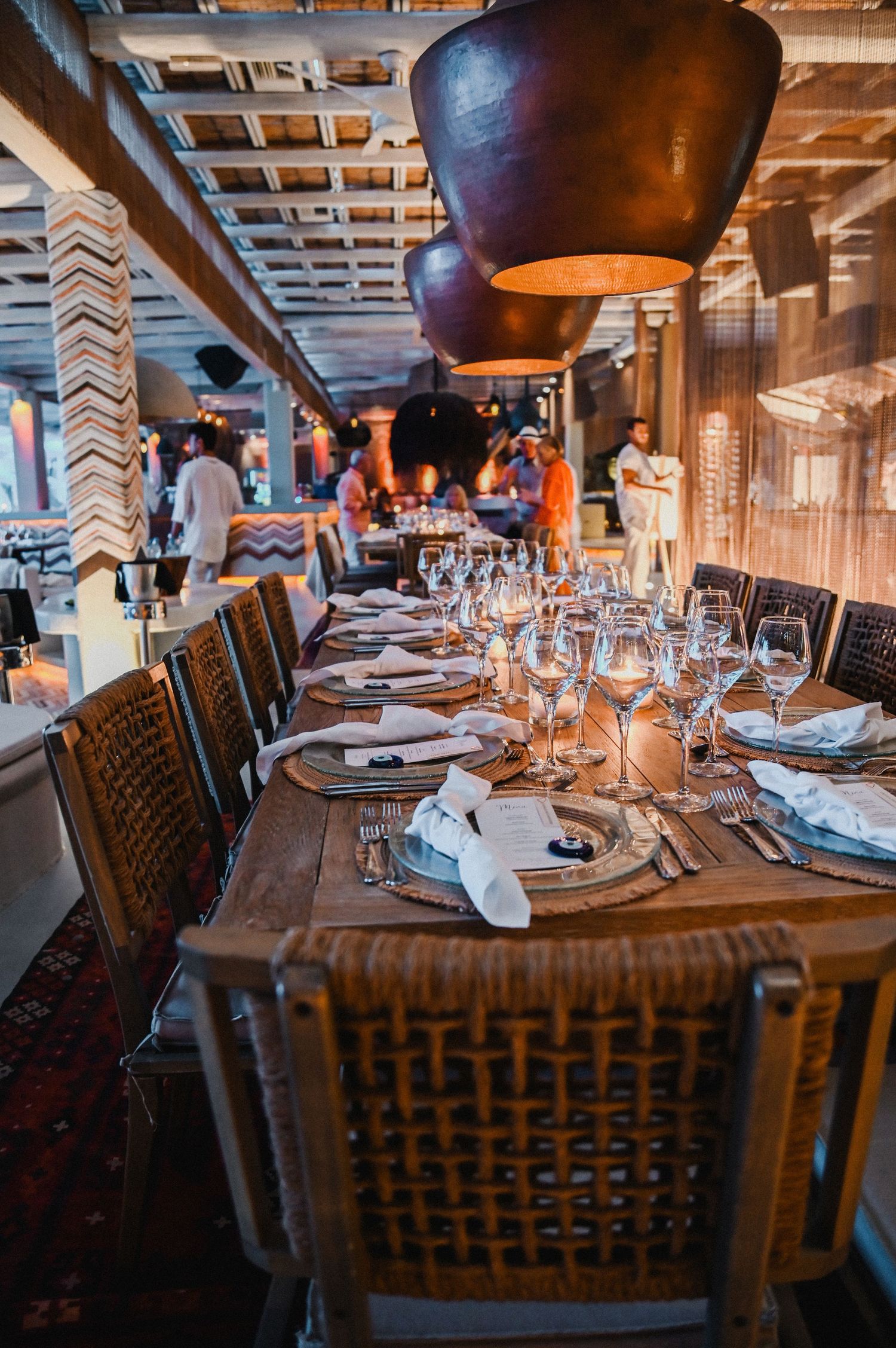 Long dining table with rattan chairs and pendant lights set for elegant wedding reception.