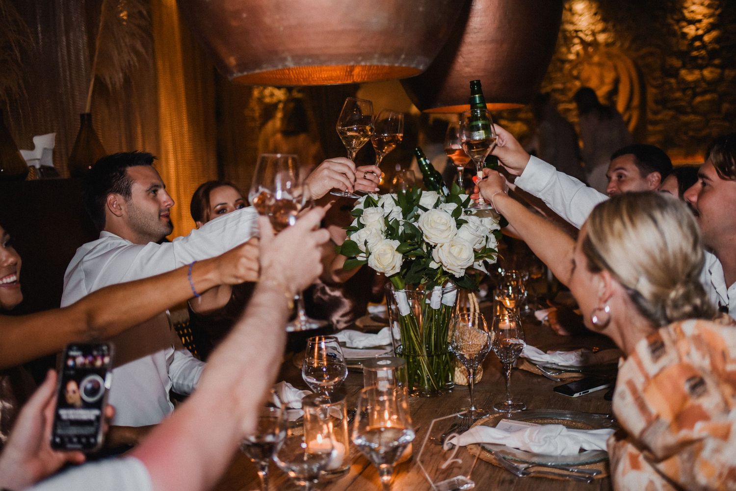 Wedding guests raising glasses for a toast at an intimate candlelit dinner table.