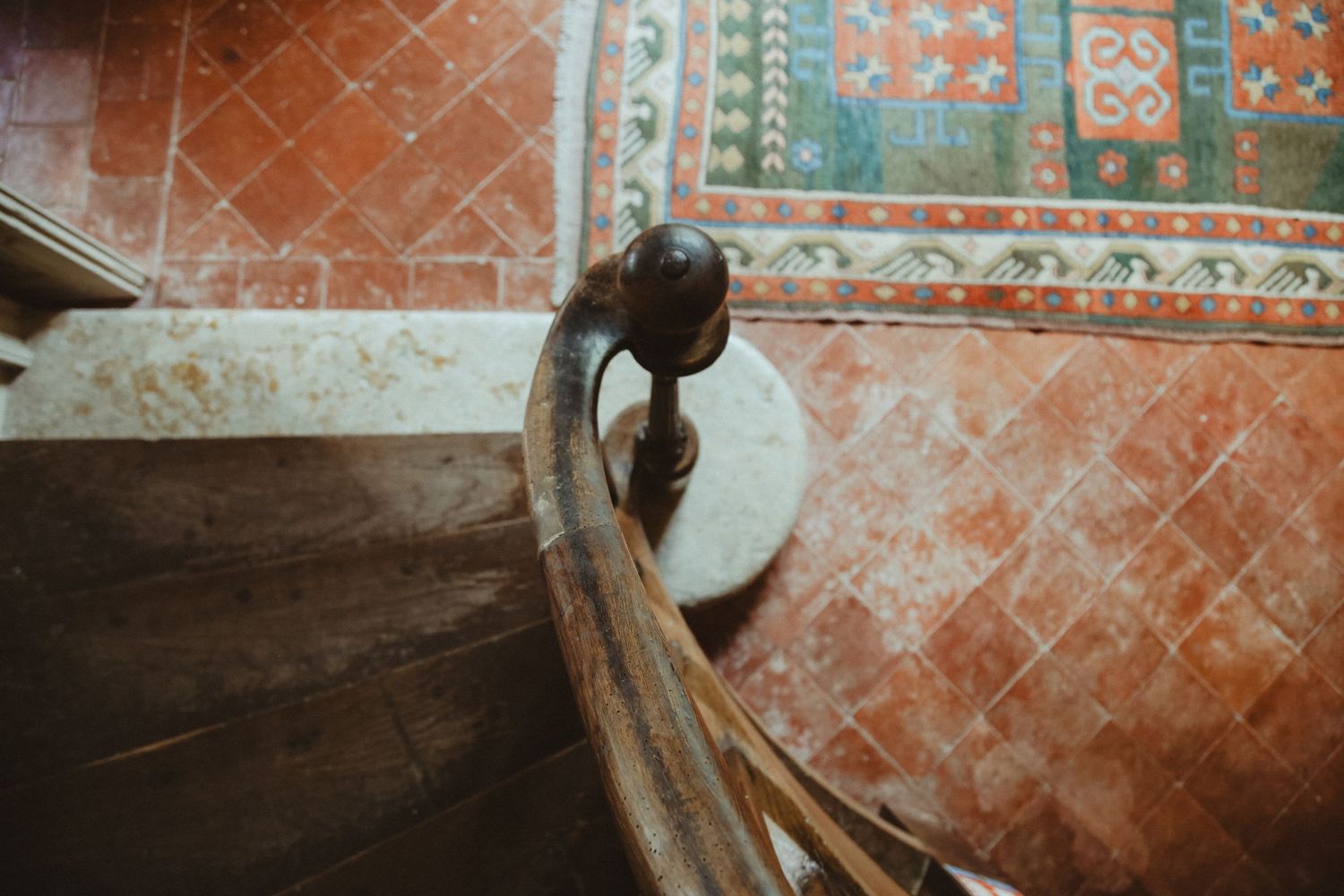Close-up of a curved wooden banister against a terracotta wall and patterned carpet.