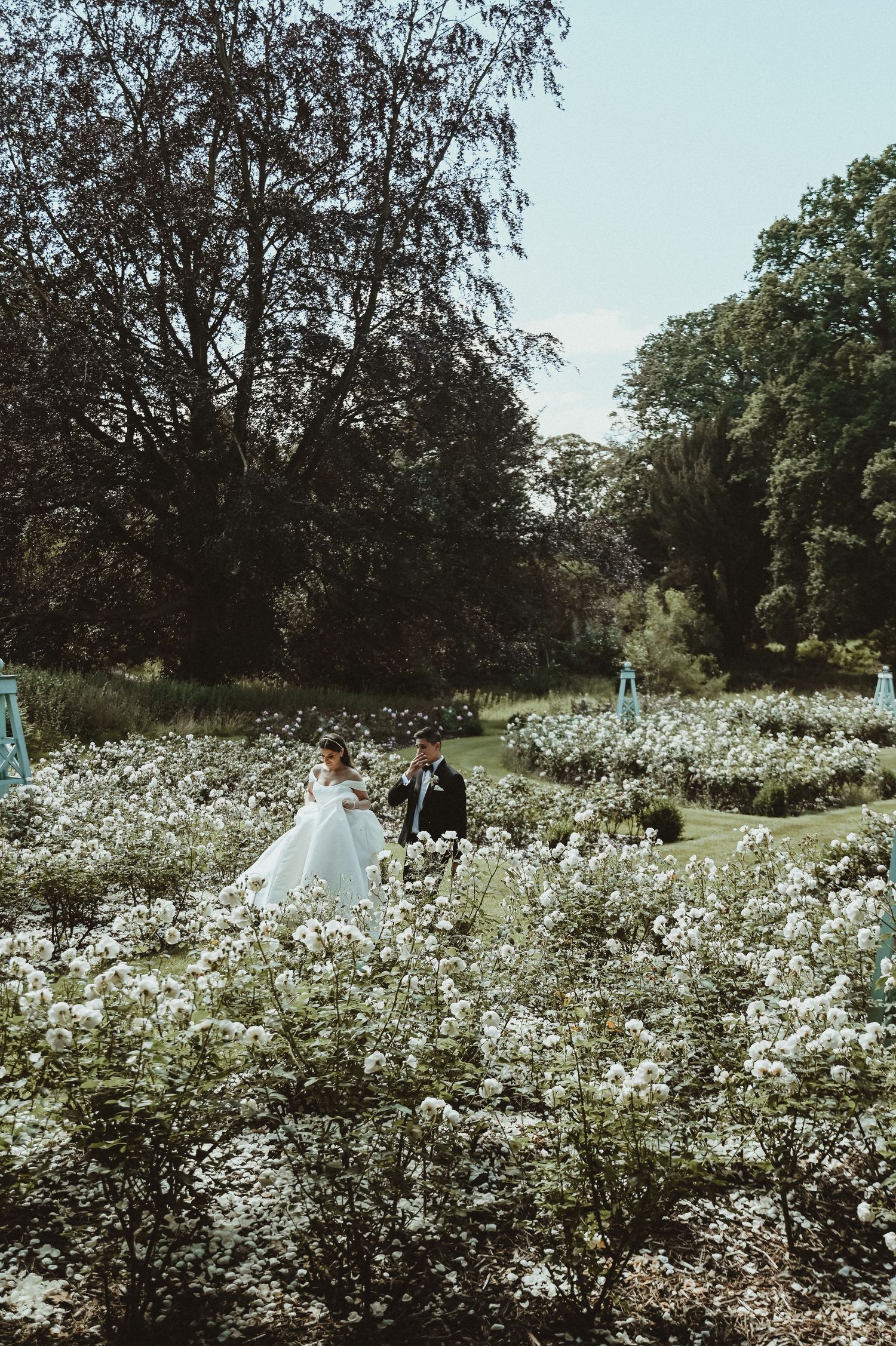 A couple stands in a lush garden filled with blooming white flowers on their wedding day.