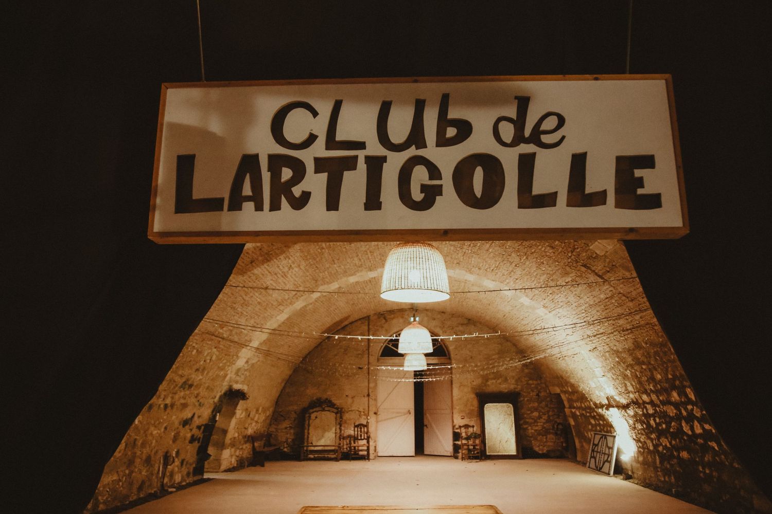 An illuminated underground stone cellar with 'Club de Lartigolle' sign above the entrance.
