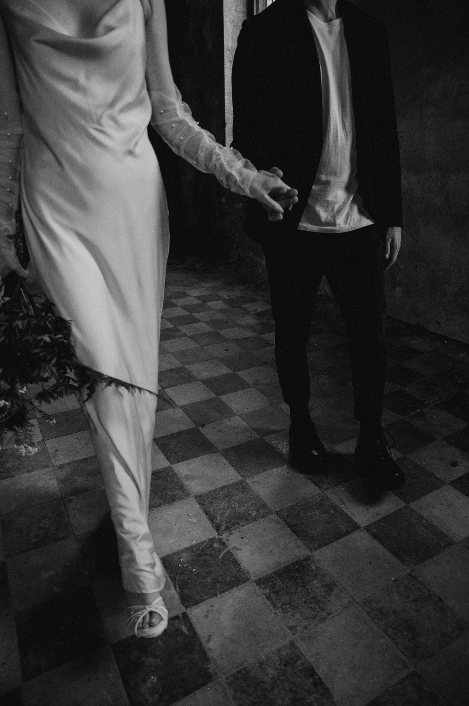 Two people in contrasting outfits stand on a vintage checkered floor in a dark, atmospheric setting.