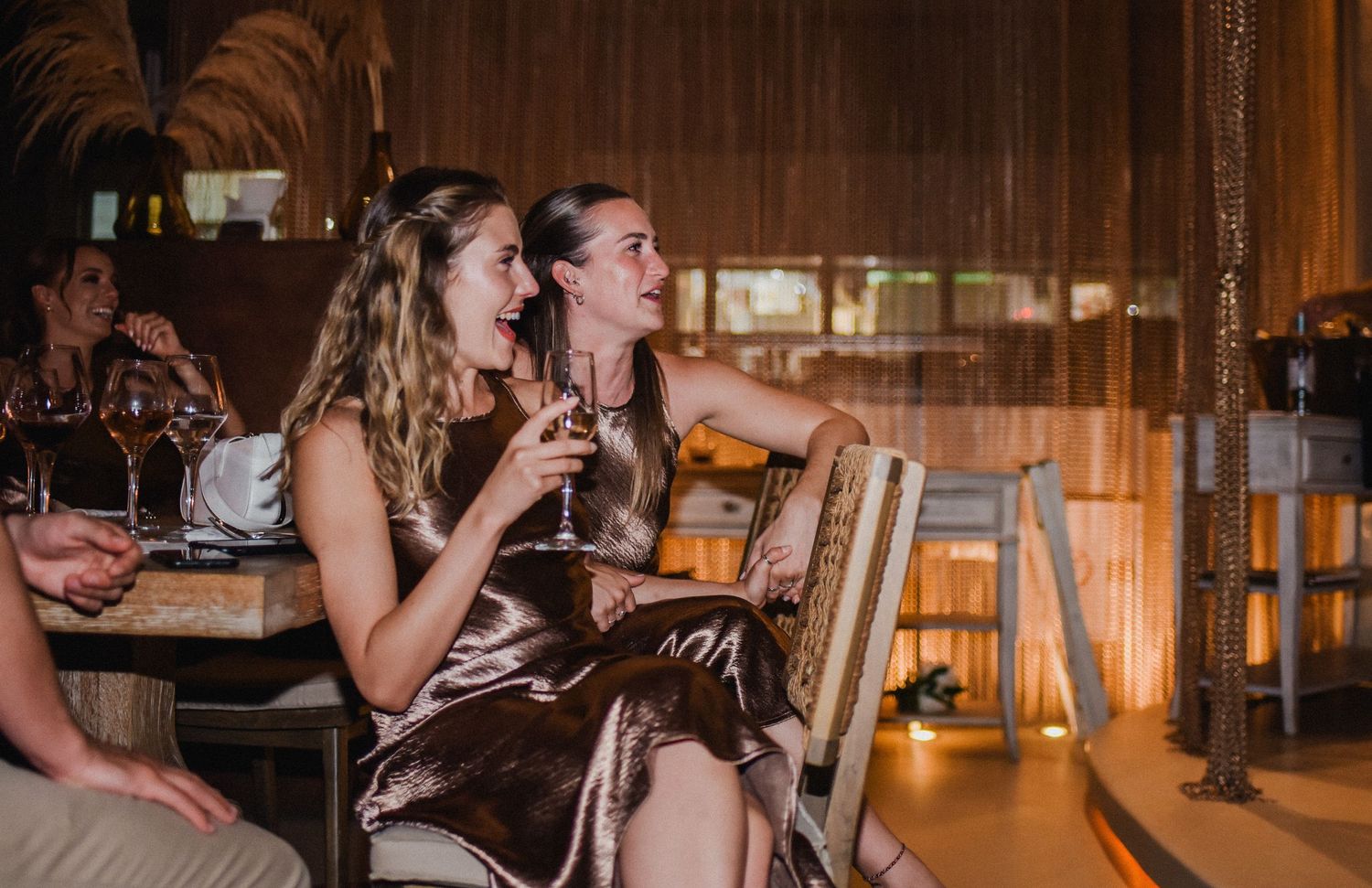 Friends enjoying drinks and laughter at a warmly lit restaurant bar.