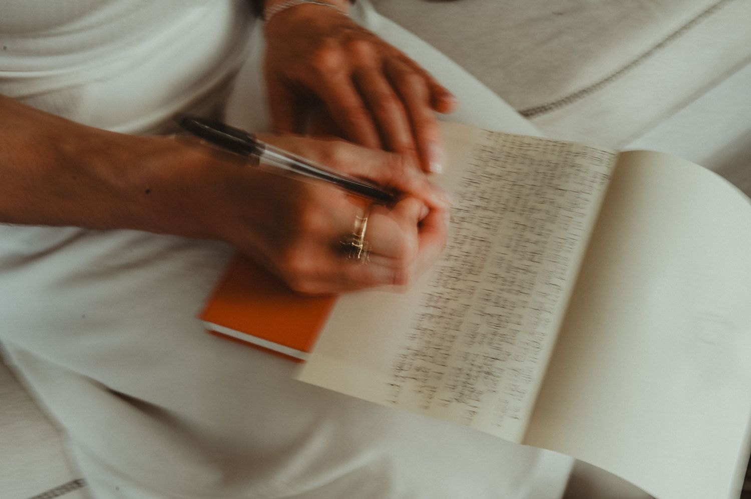 Hand wearing wedding ring writes in journal against white background in intimate setting.