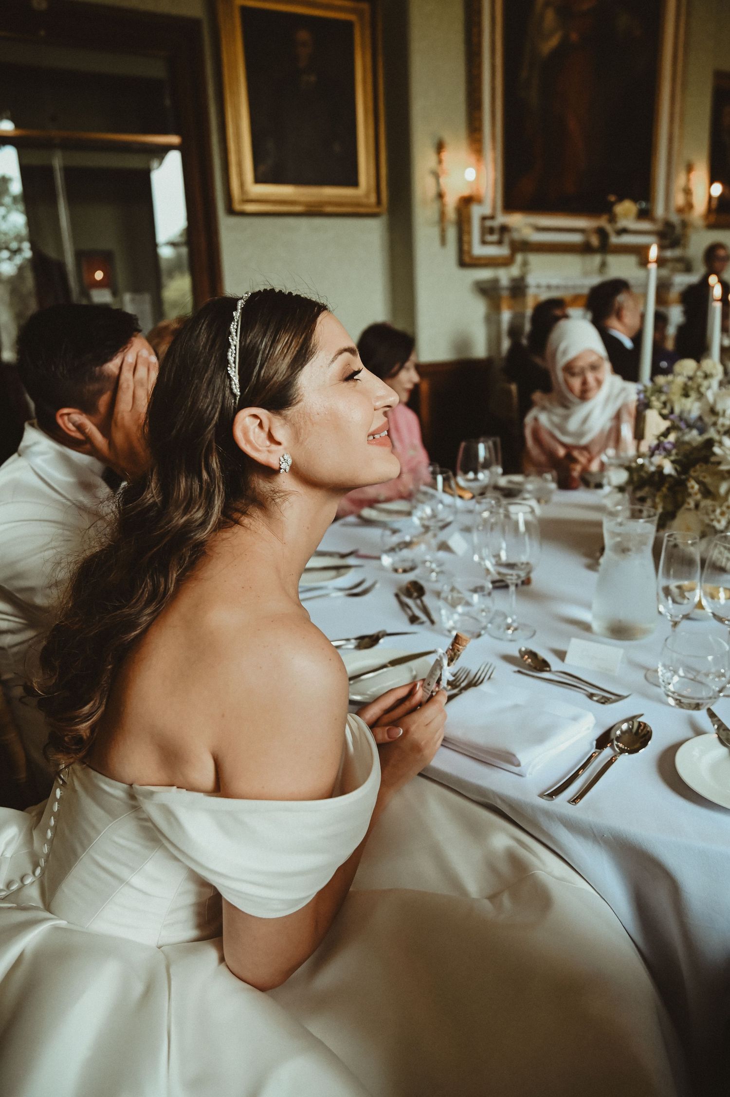Elegant wedding reception with guests seated at formal dining table with floral centerpieces.