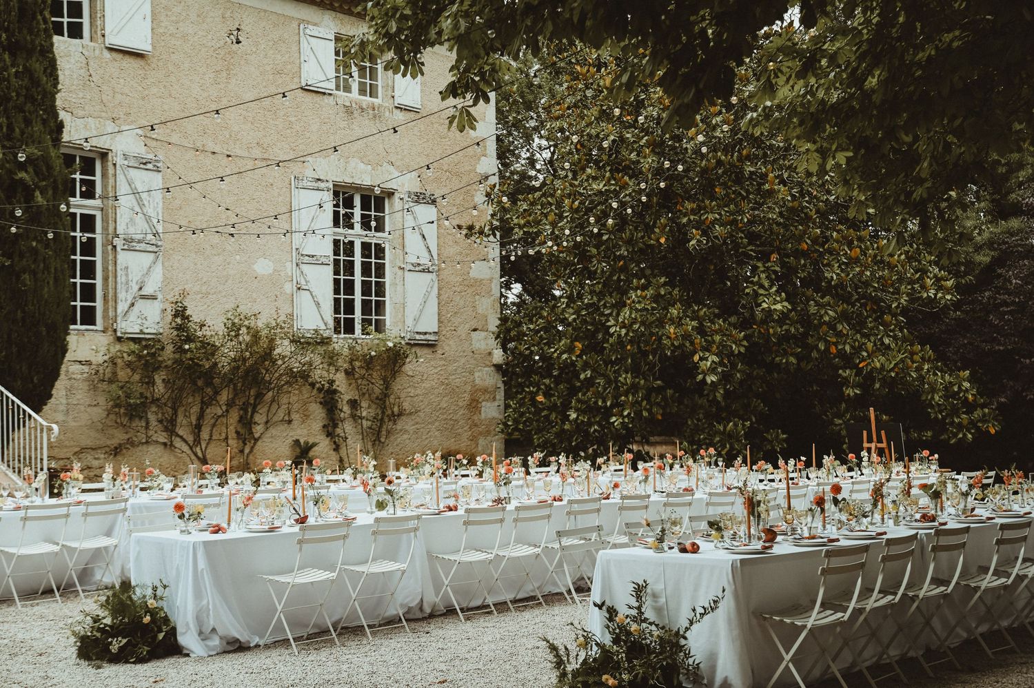 Long banquet tables set for an outdoor wedding reception at a historic French estate.