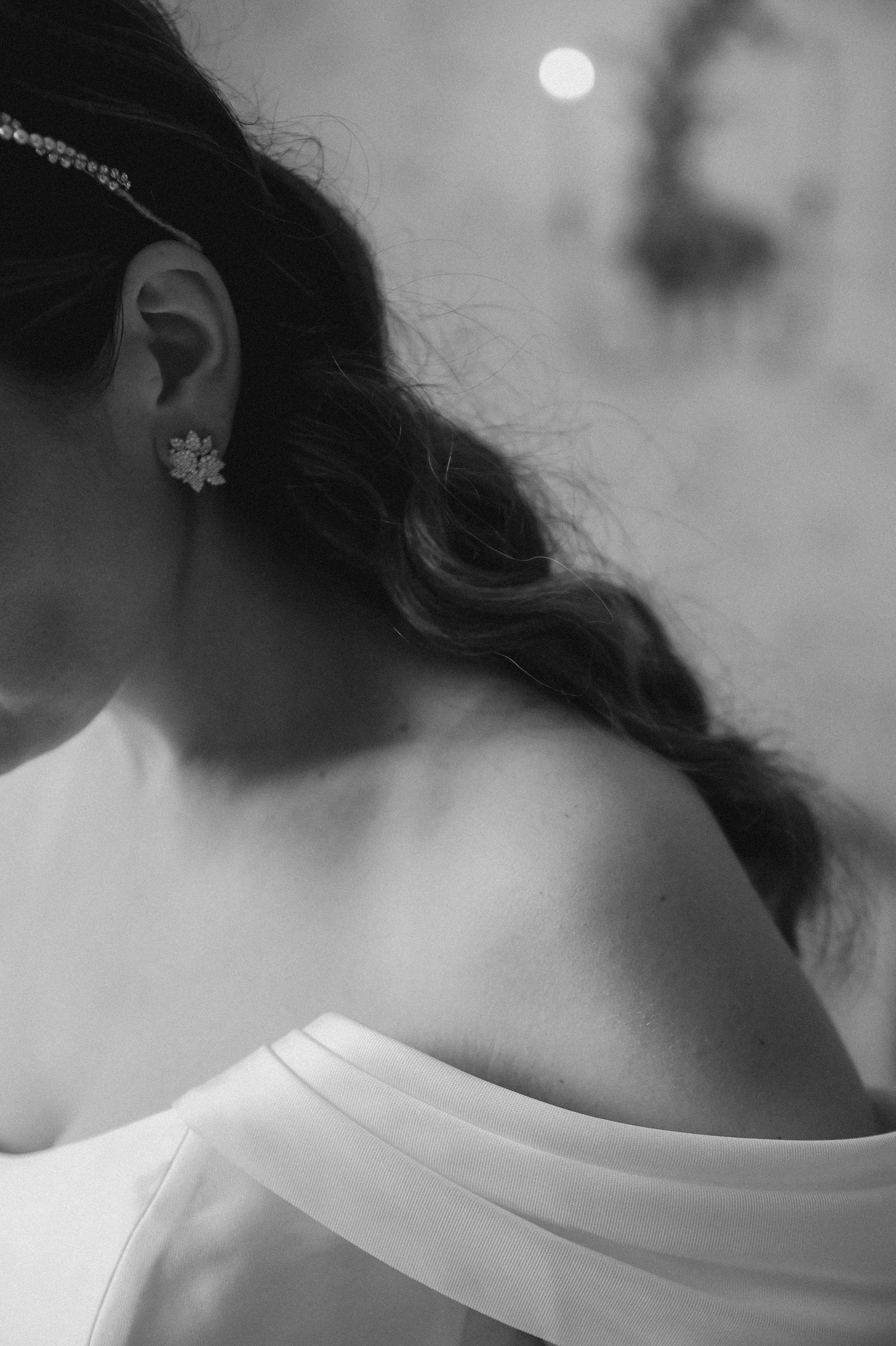 Artistic black and white detail of a floral earring and off-shoulder wedding dress.