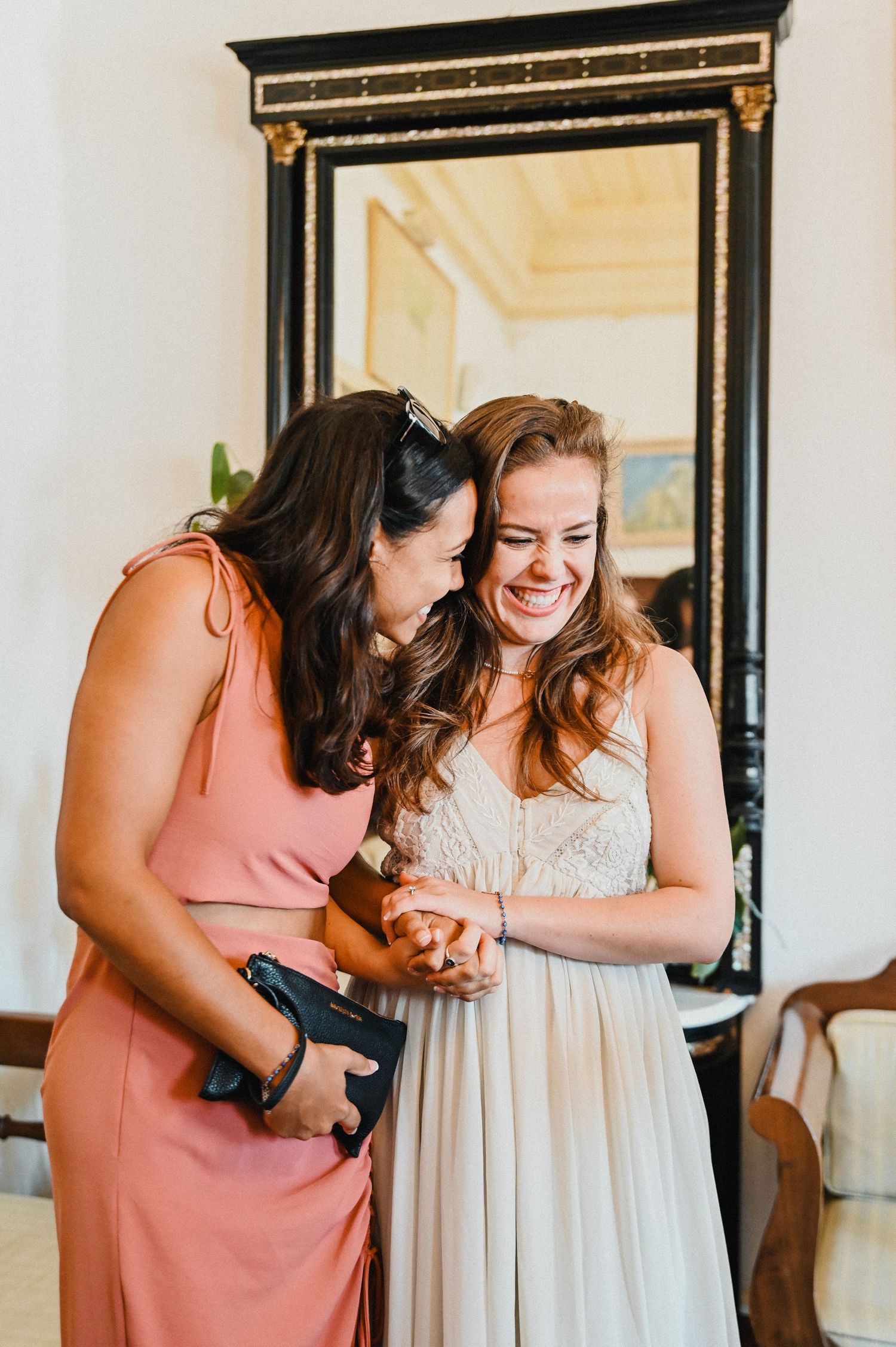 Two people share a joyful moment in front of an ornate mirror.
