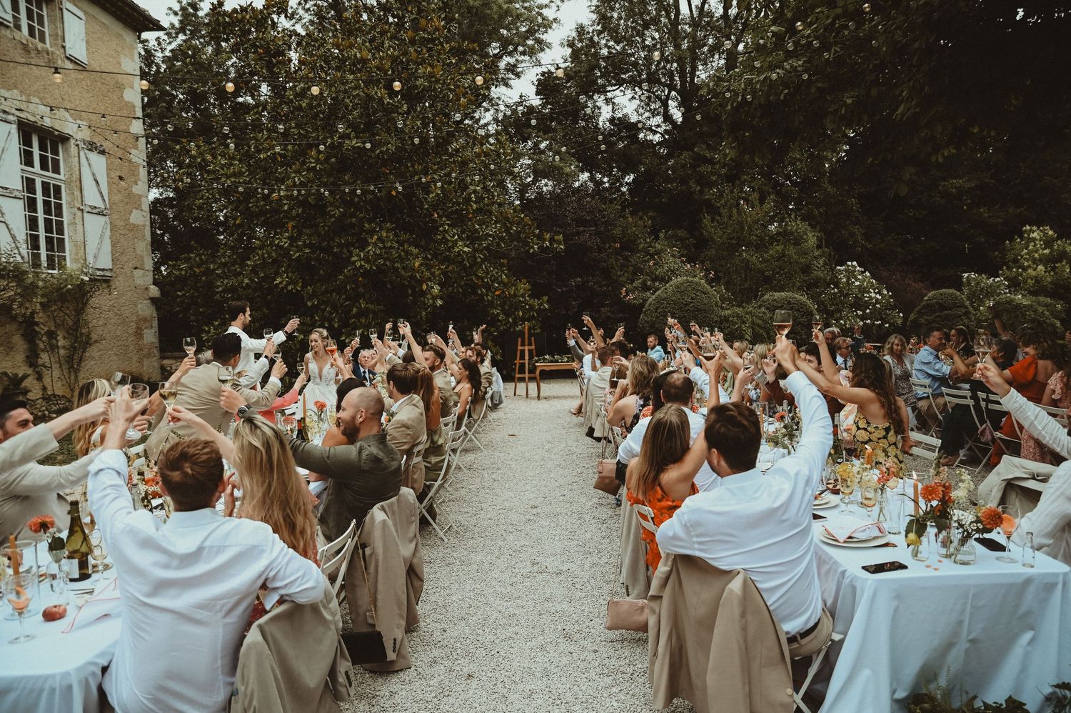 Wedding guests raise their hands in celebration during an outdoor reception with decorated tables.