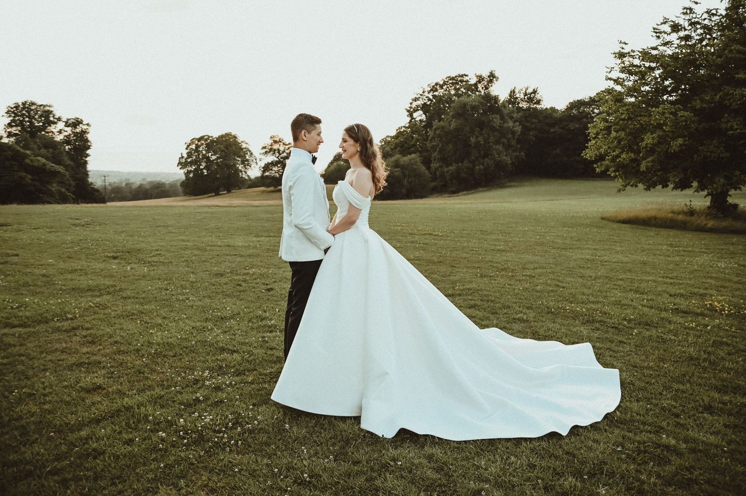 A couple embraces on a scenic hilltop in wedding attire during golden hour.