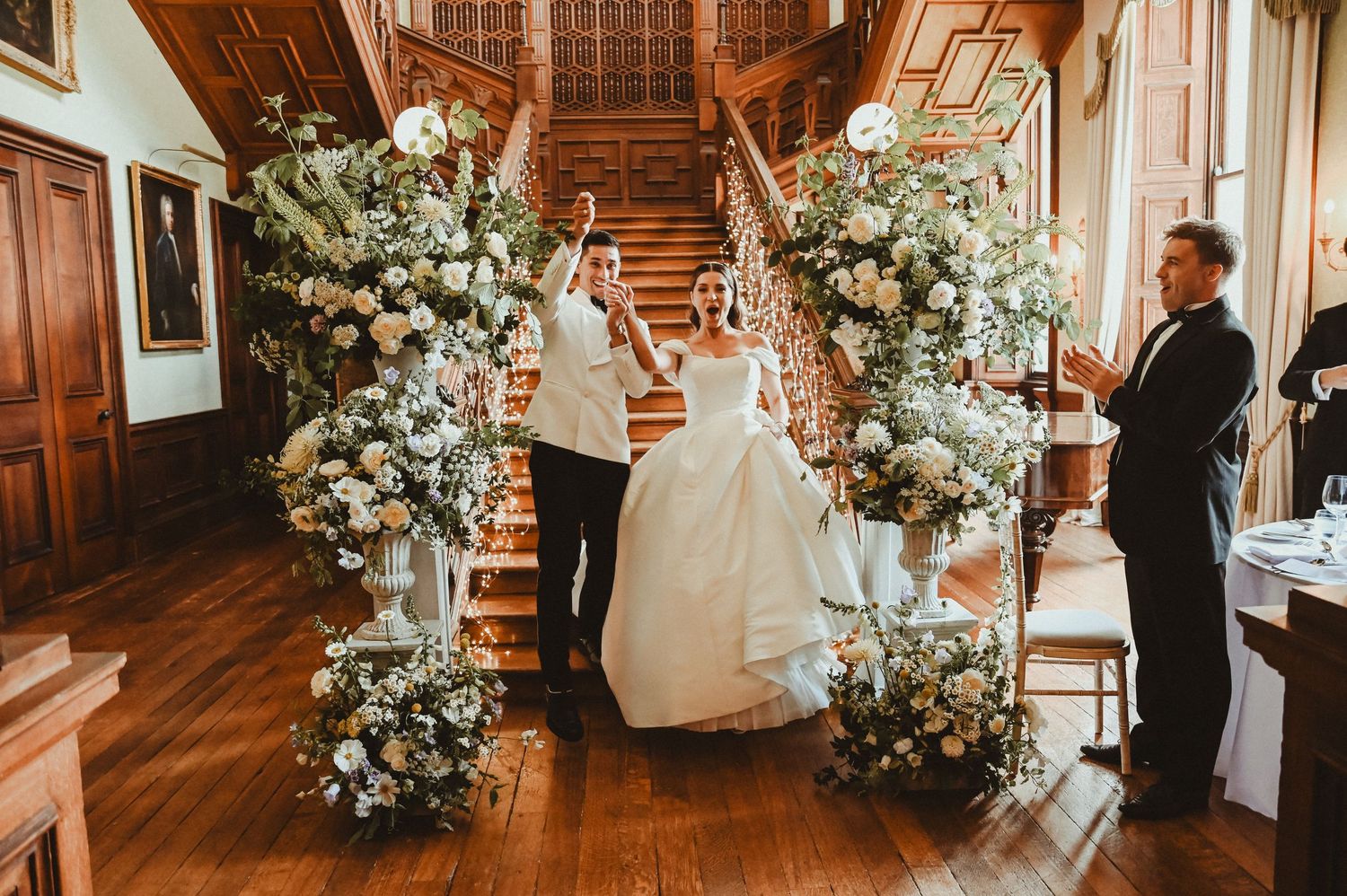 Elegant wedding staircase decorated with lush white floral arrangements and greenery in a historic venue.