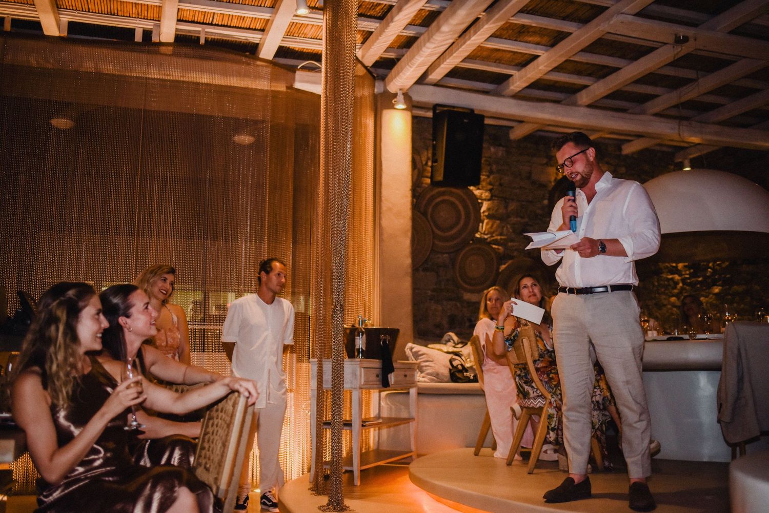 Speaker addresses audience during an evening event in a rustic wooden venue.