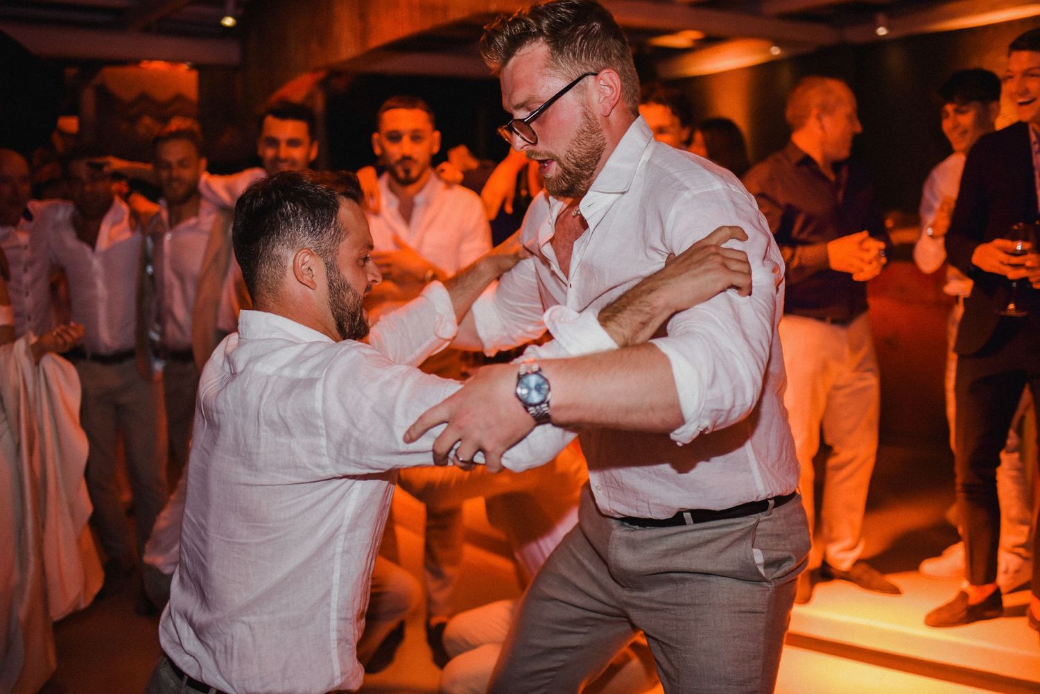 Wedding guests dancing and celebrating on illuminated dance floor.