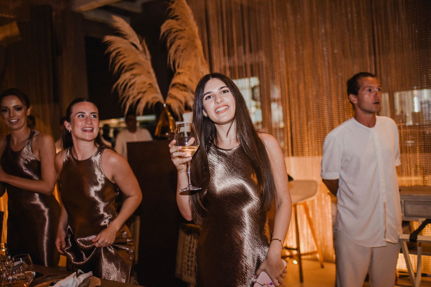 Wedding guests dancing and celebrating with feather props in a warmly lit venue.