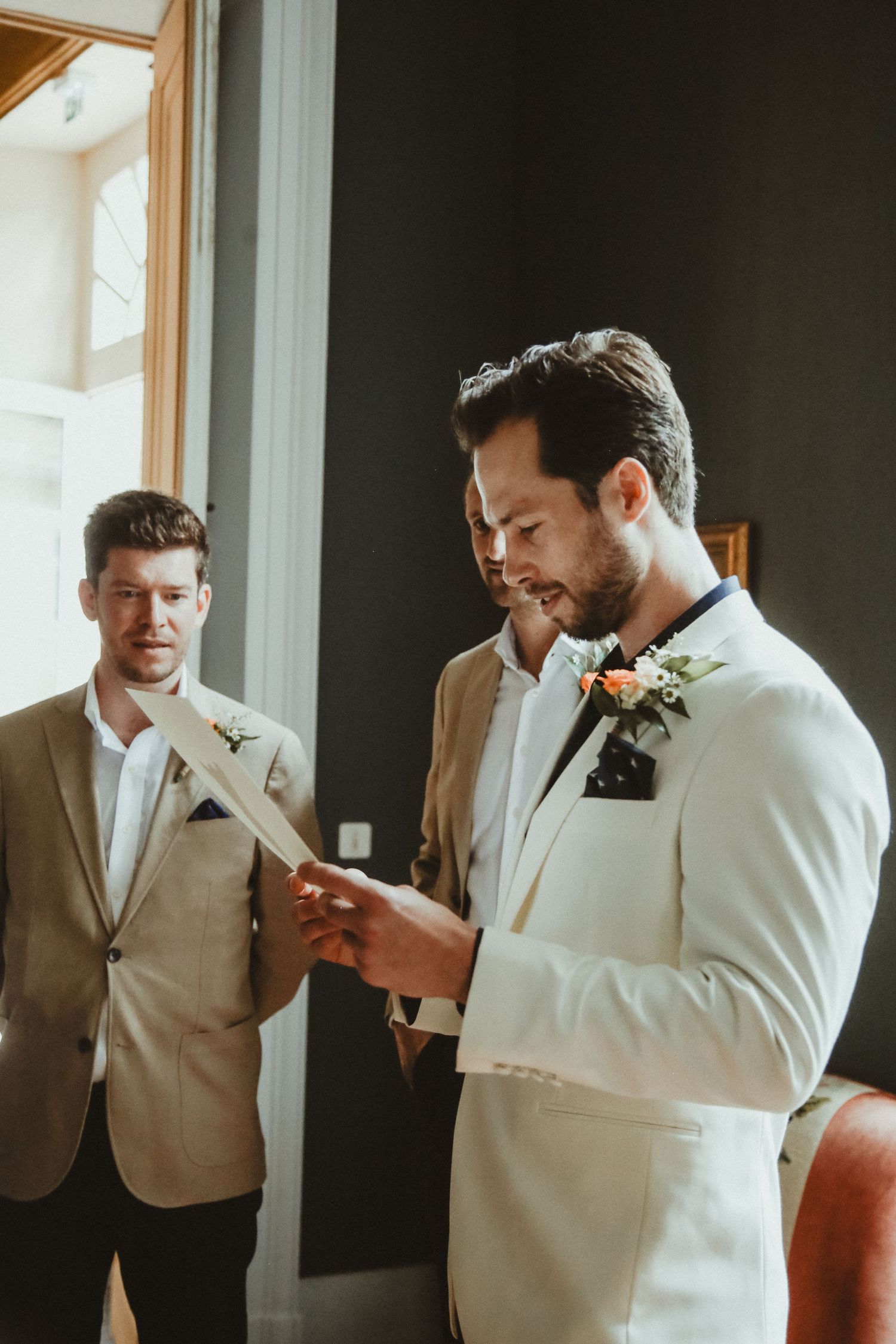 Two men in formal attire reviewing documents during wedding preparations.
