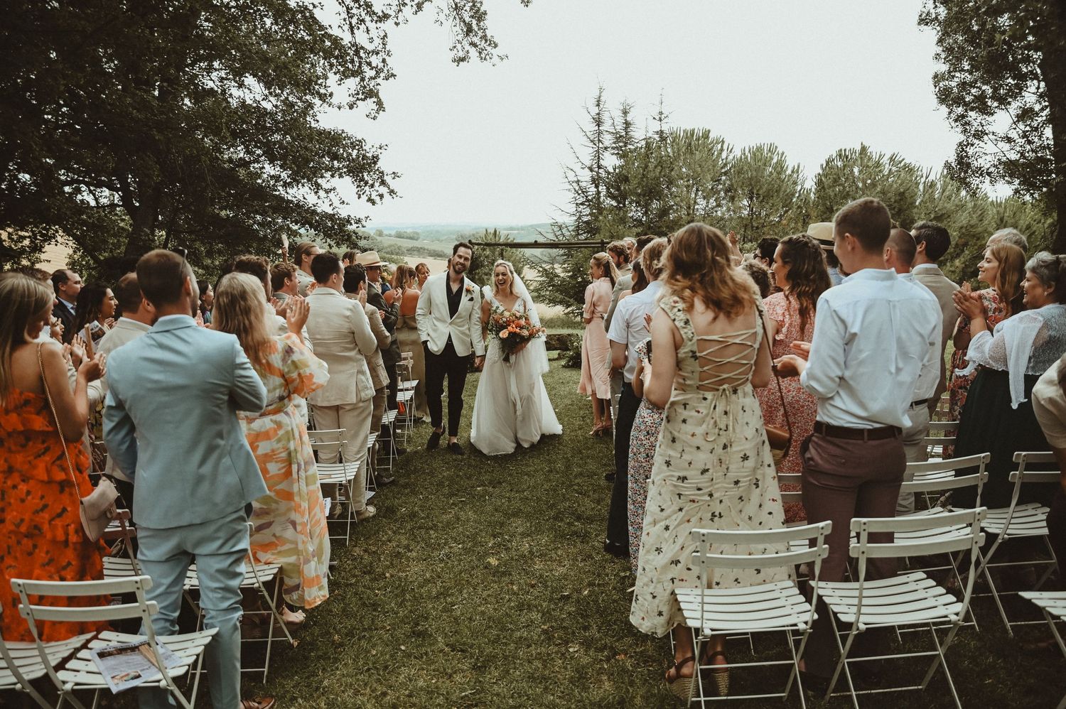 Wedding guests stand during the recessional at an outdoor ceremony with folding chairs.