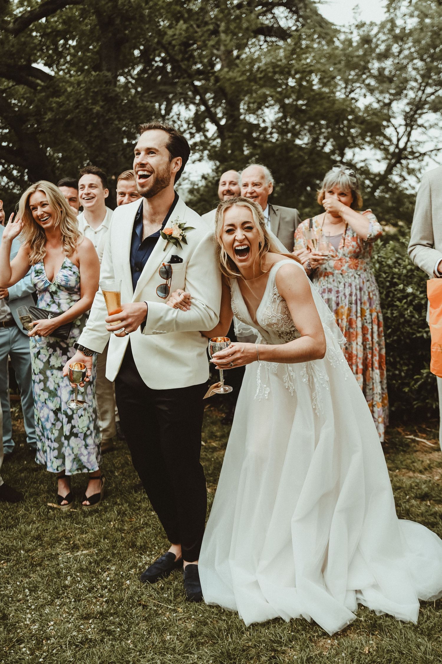 Wedding guests laugh and celebrate outdoors during a joyous reception.