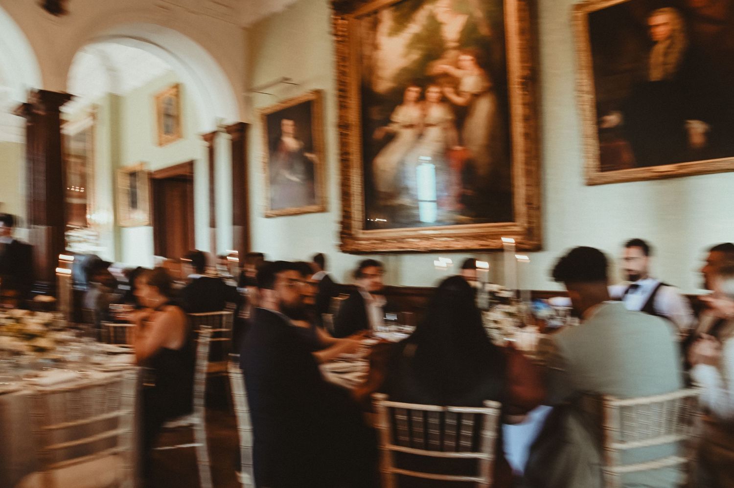 Wedding guests dining beneath historic portraits in an elegant mansion reception hall.