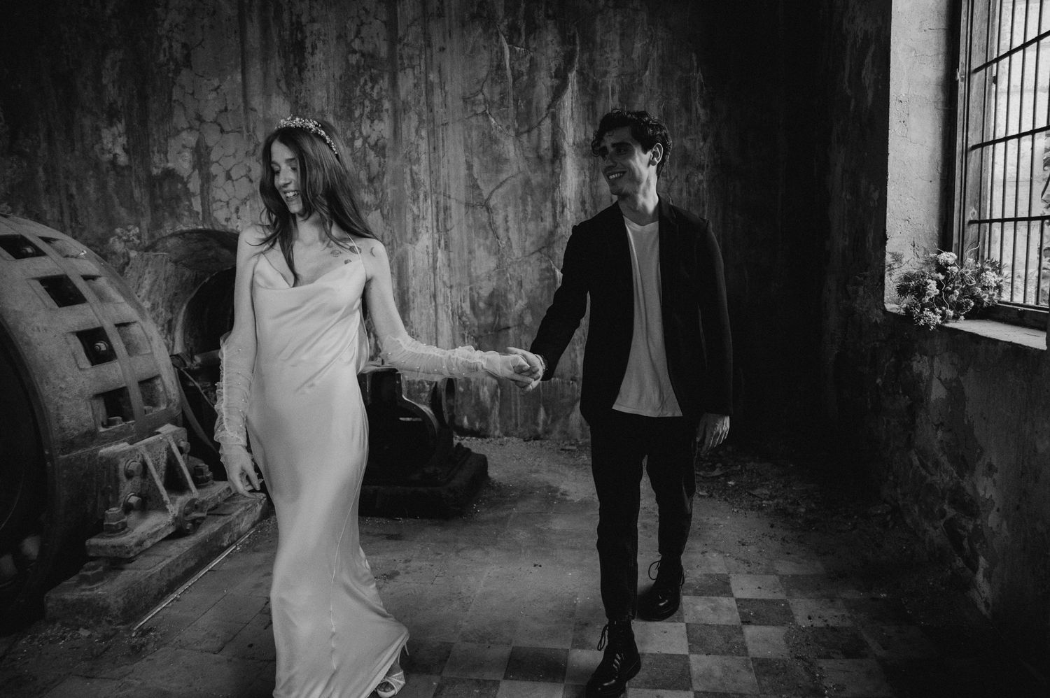 A couple walks through an industrial space with distressed walls and checkered flooring.