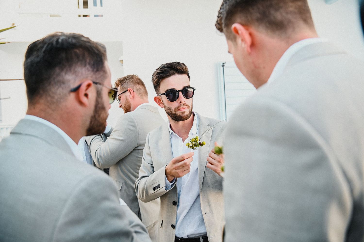 Groomsmen in light gray suits socializing during outdoor wedding event.
