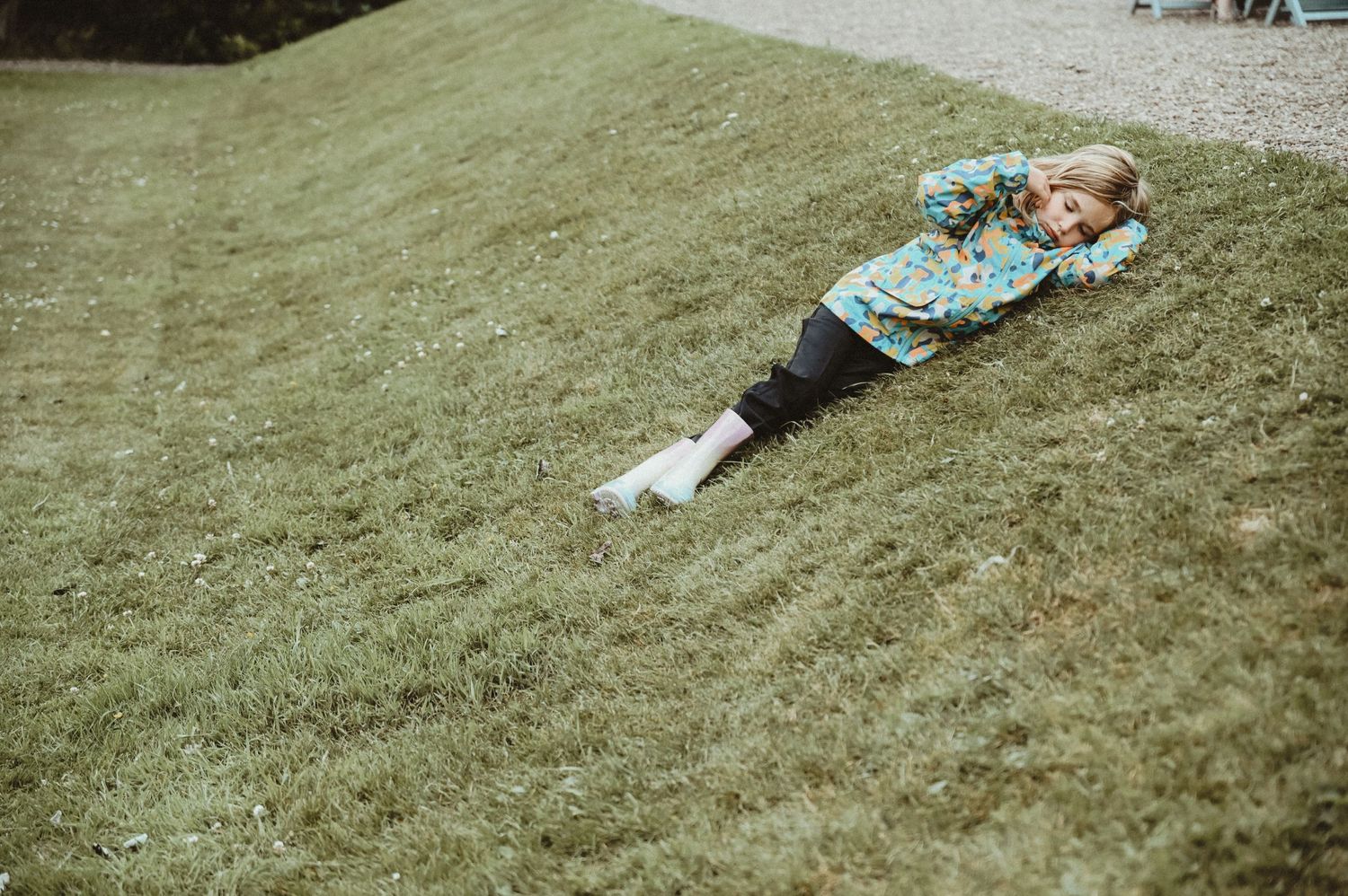 A person lies on a grassy hillside enjoying a lazy afternoon in casual attire.