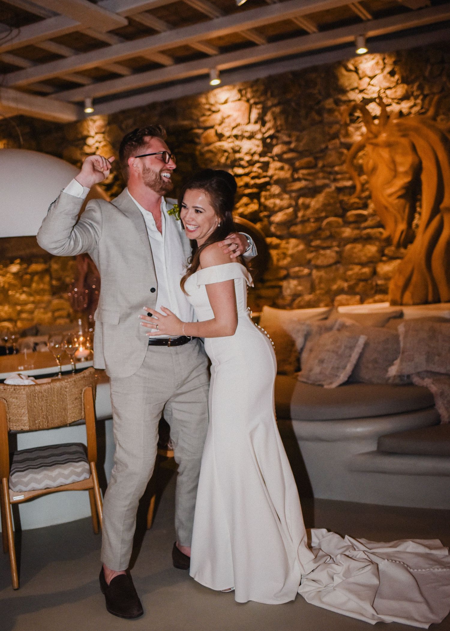 Newlyweds sharing a joyful dance moment in a rustic venue with exposed stone walls and wooden beams.