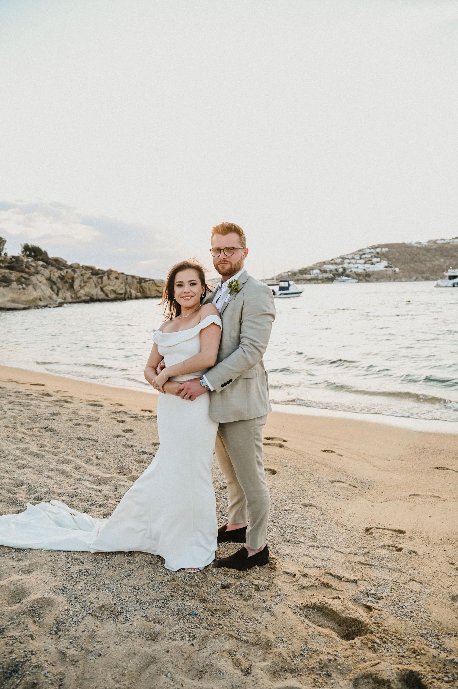 A couple shares a romantic moment on a beach with rocky cliffs and ocean views during their wedding photoshoot.