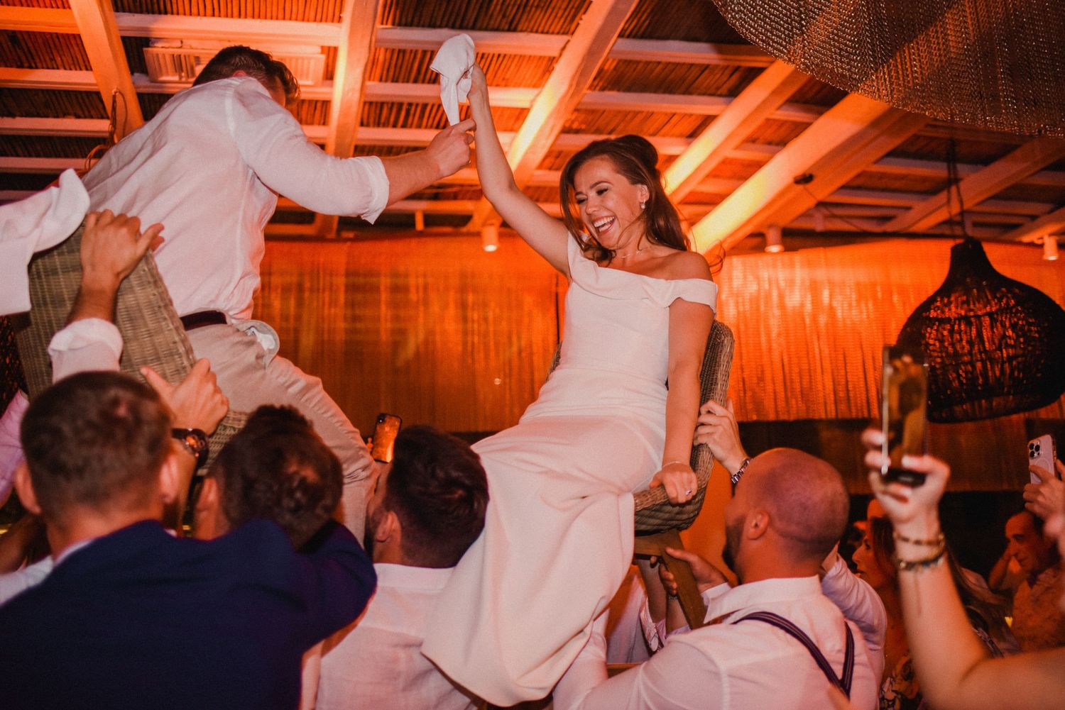 Wedding guests lift the newlyweds on chairs during traditional celebration dance.