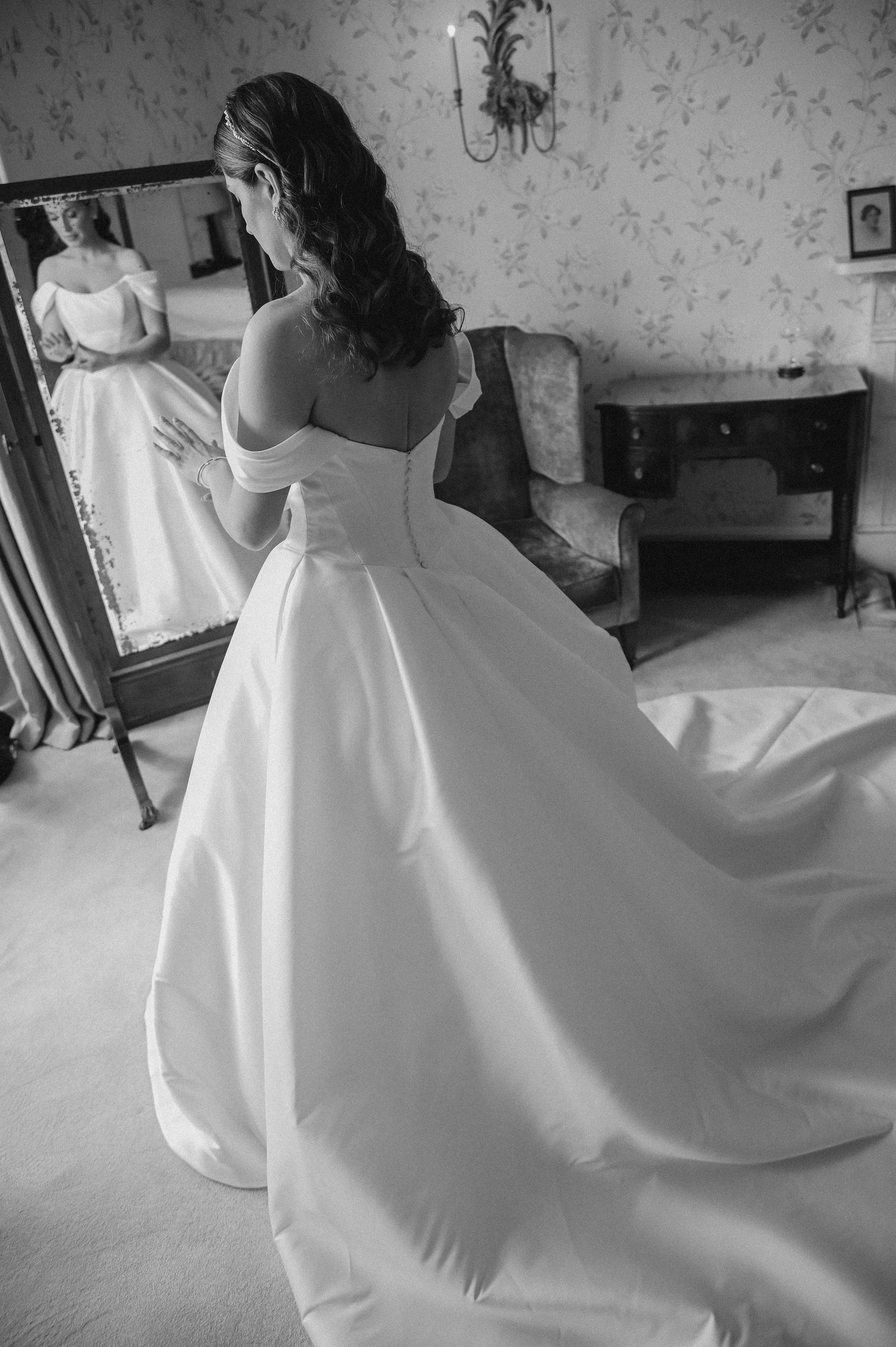 Black and white photo of a wedding dress reflection in a full-length mirror.