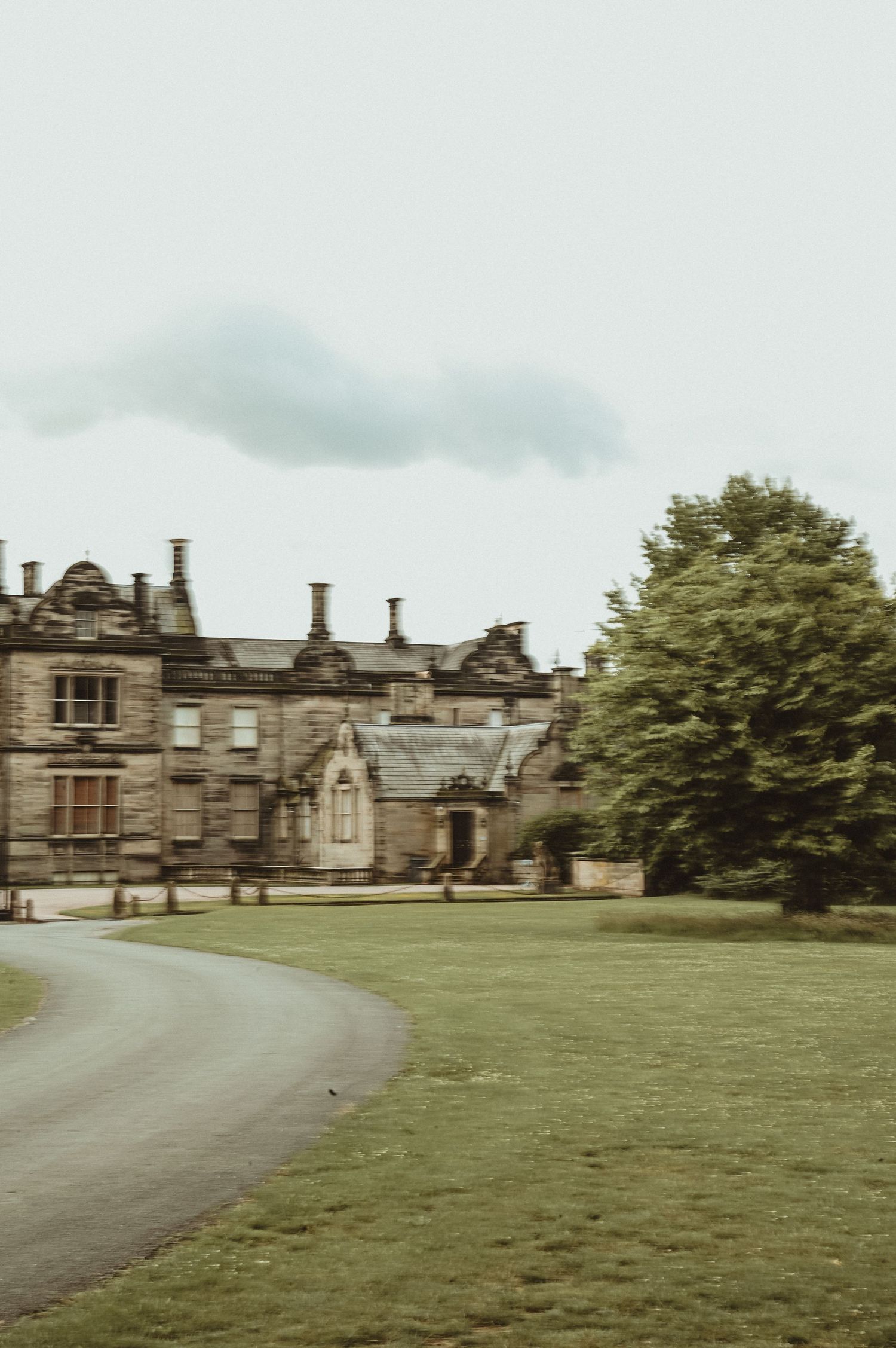 Historic manor house with Gothic architecture set against lush green grounds and a curved driveway.