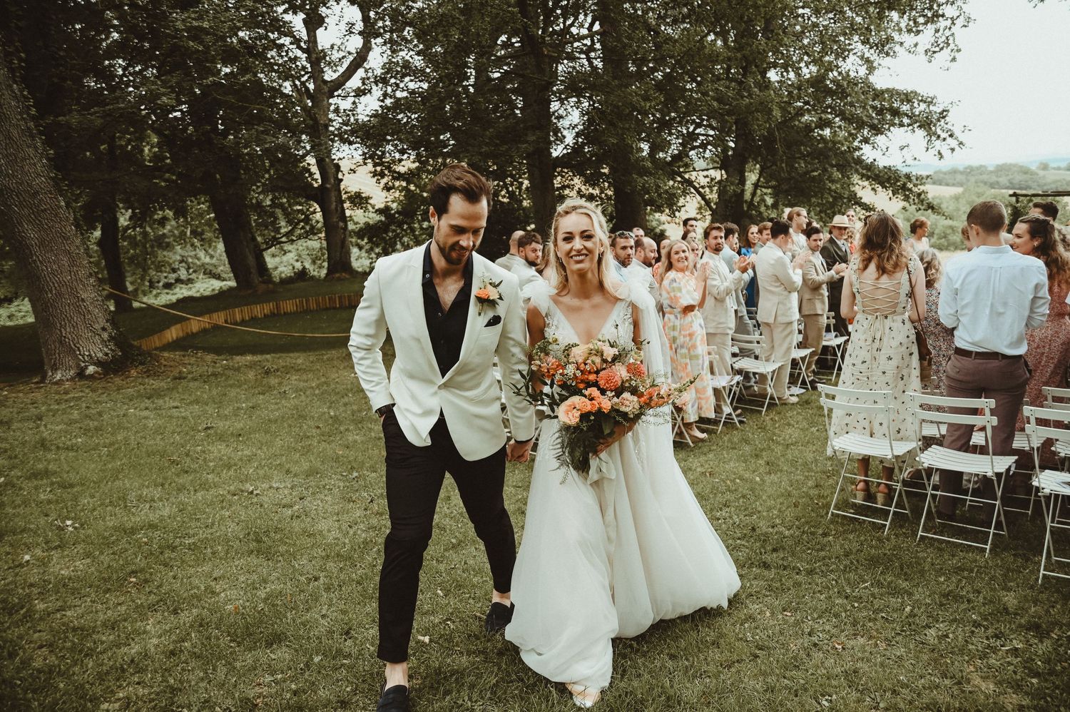 A couple walks down the aisle during their wedding recessional in a garden setting.