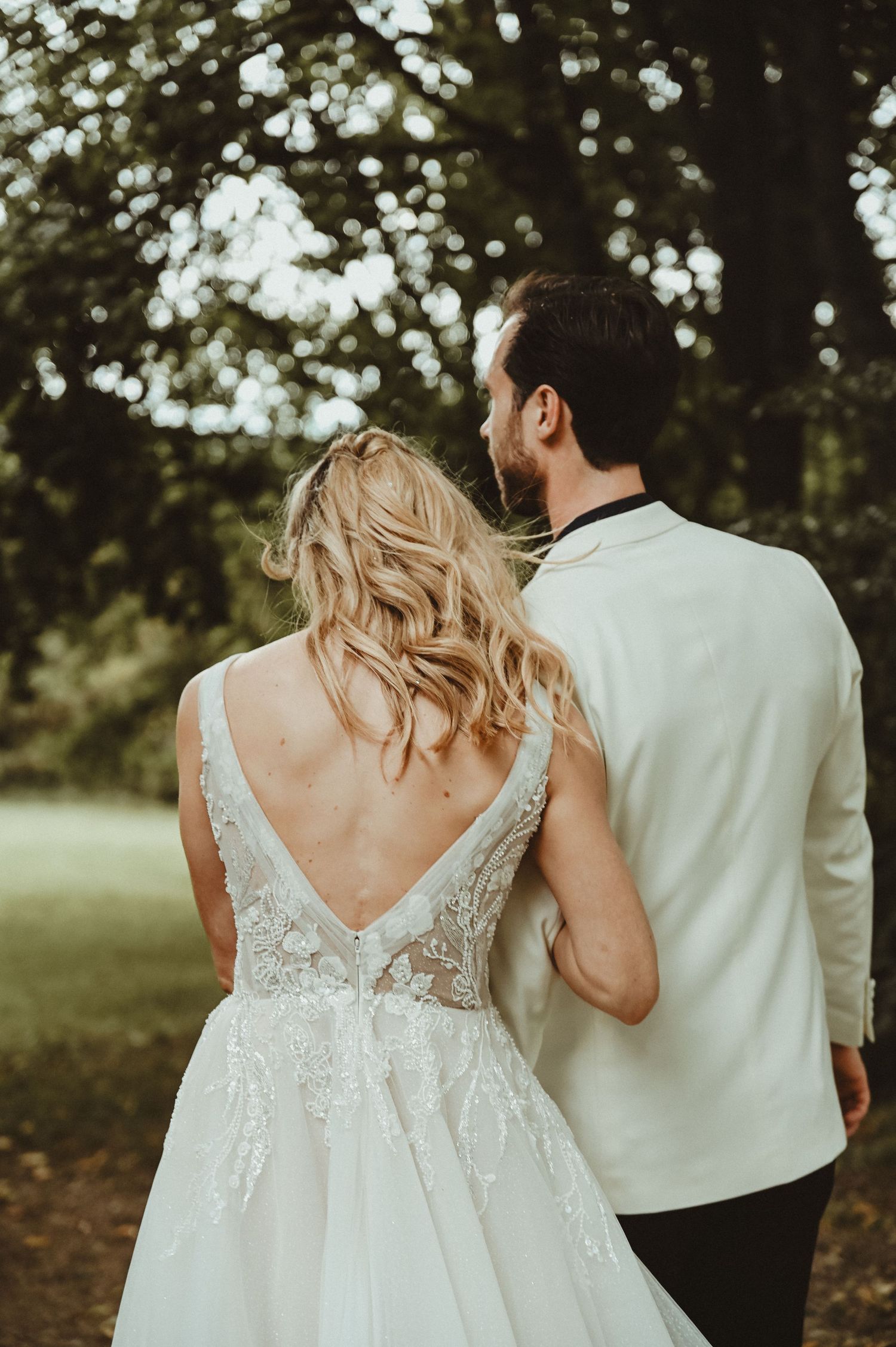 A close-up view of a bride's detailed lace back wedding dress as the couple stands together outdoors.