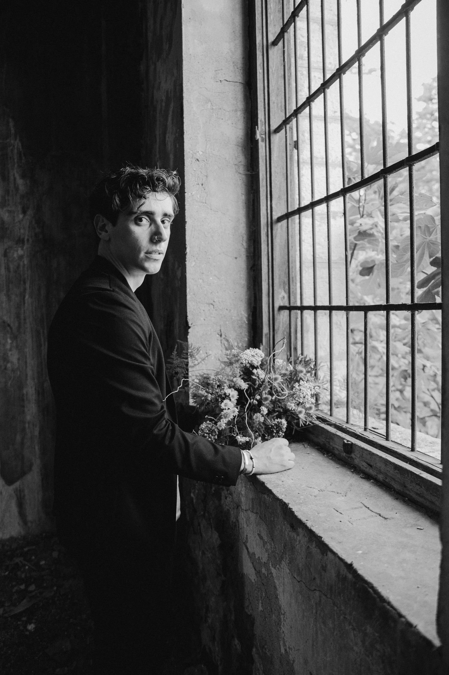 Dramatic window-lit portrait with person holding delicate floral bouquet in dark room.