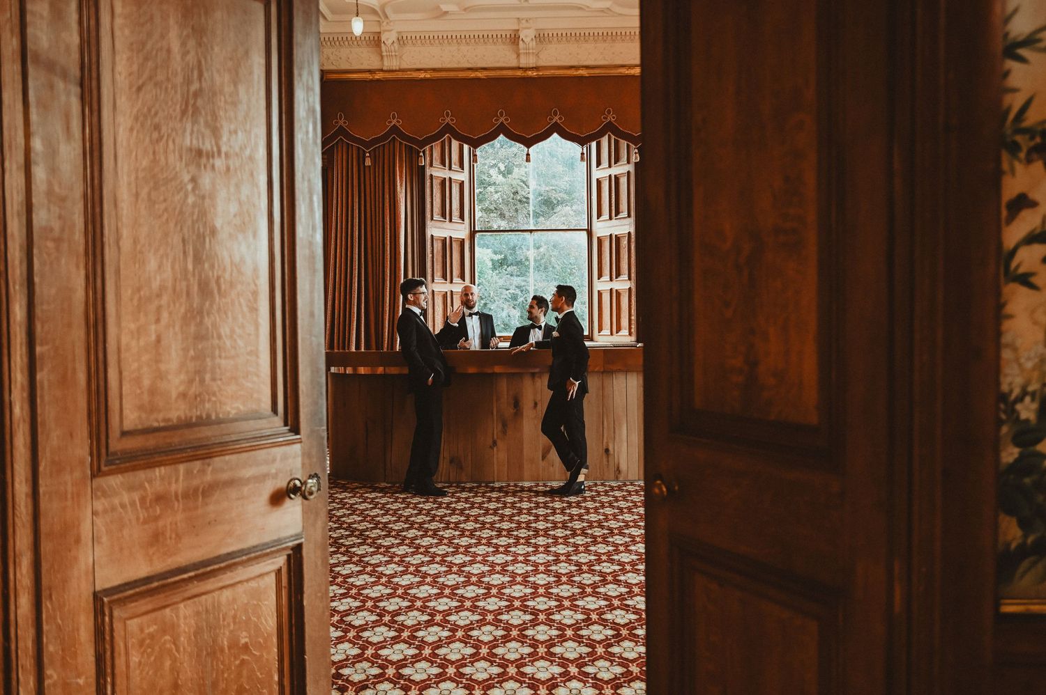 View through wooden doors into an ornate room with patterned floor and window alcove.