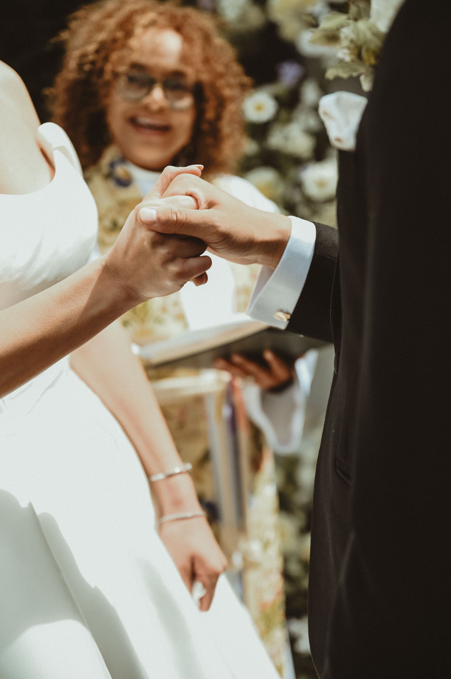 Close-up of wedding rings being exchanged during an outdoor ceremony with floral decorations.