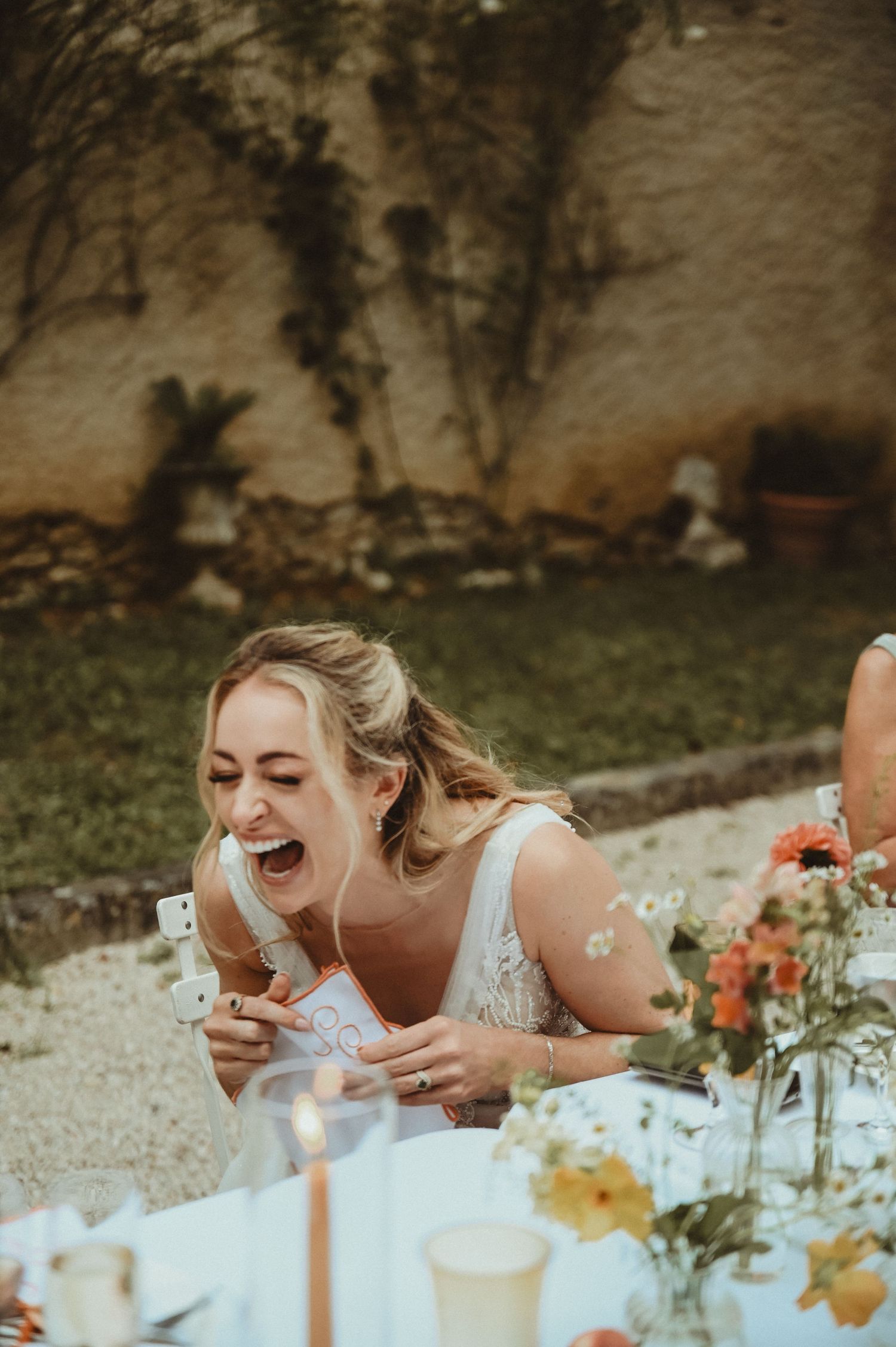 Joyful laughter during outdoor wedding reception with floral centerpieces and string lights.