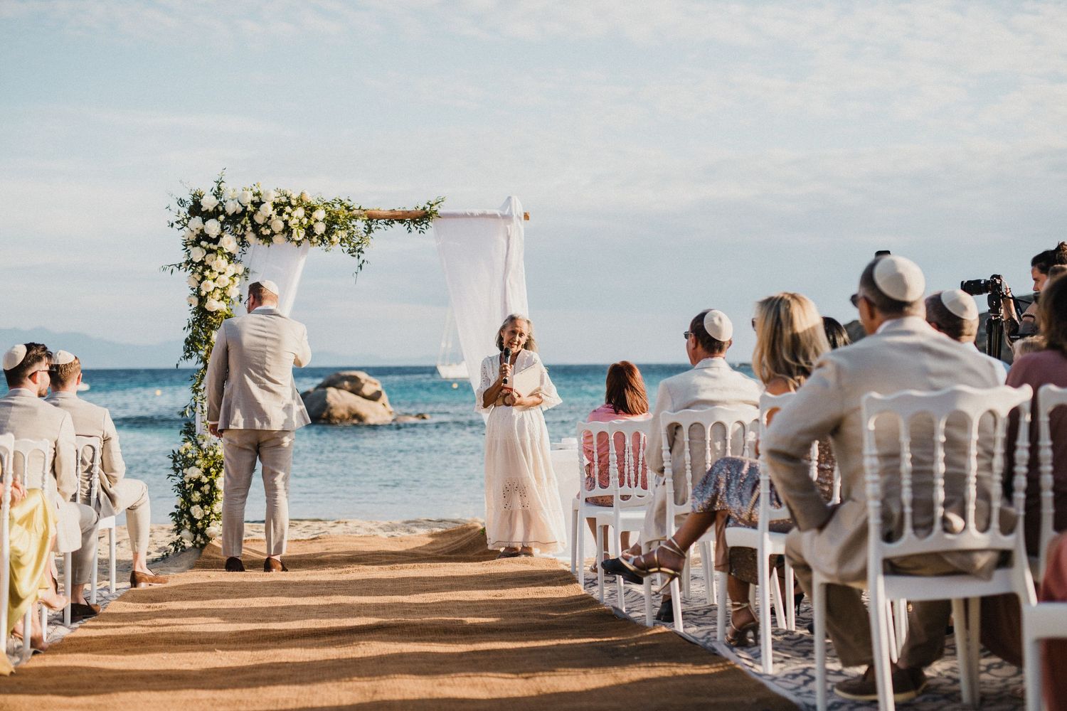 Beachfront wedding ceremony with white chairs and floral arch overlooking the ocean.