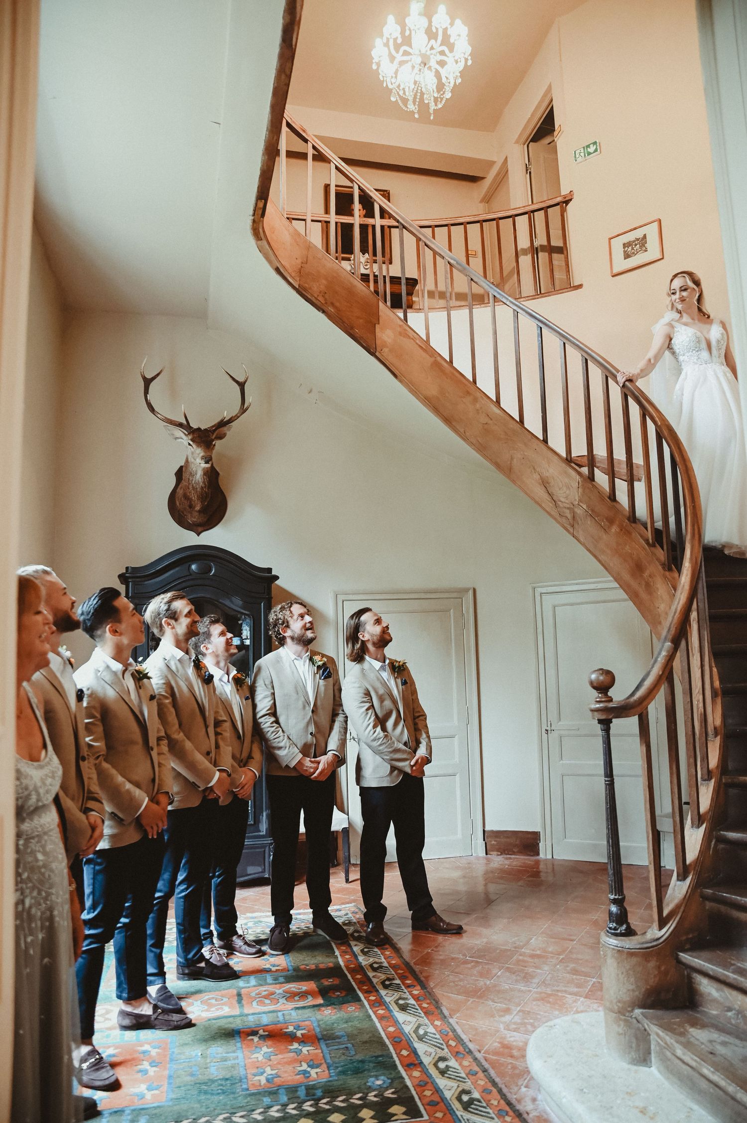 An elegant wedding first look moment on a curved wooden staircase with mounted deer head decor.