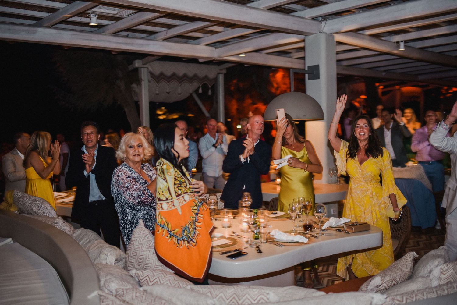 Wedding guests enjoying a lively celebration at a reception with colorful attire and buffet tables.
