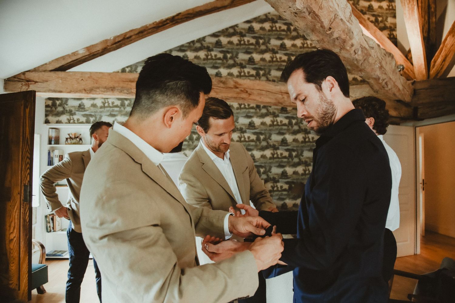Three people gather in a rustic room with exposed brick walls and wooden beams during preparations.