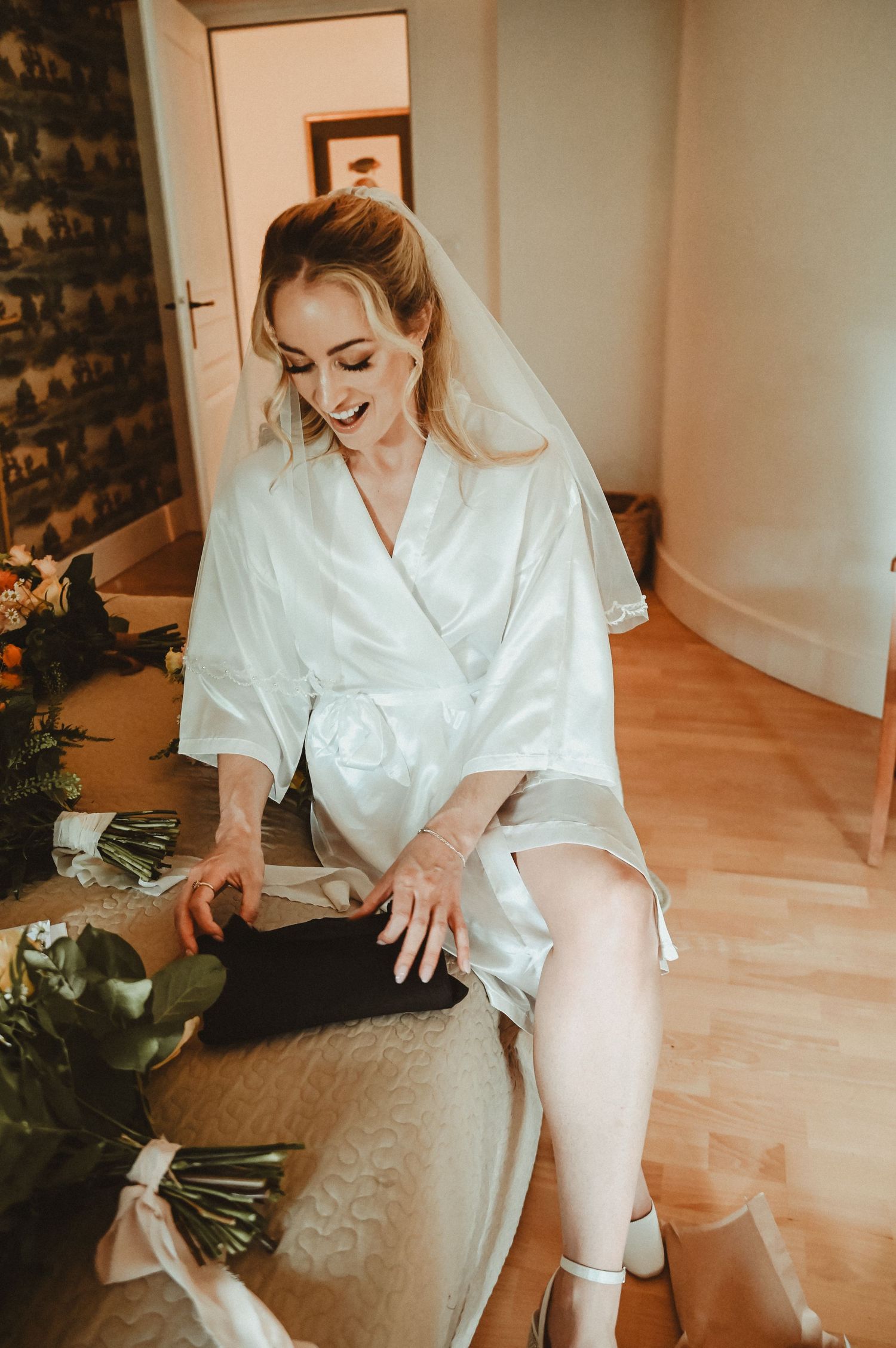 Wedding morning preparations with flowers and white silk robe in sunlit room.