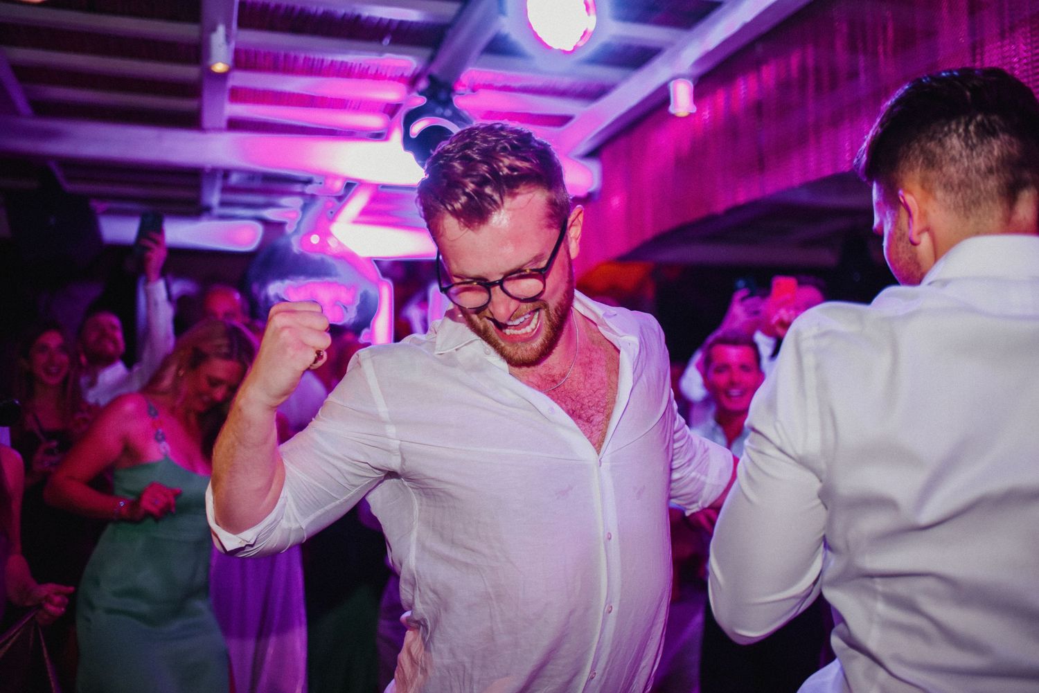 People dancing and celebrating at a nightclub with purple lighting and energetic atmosphere.