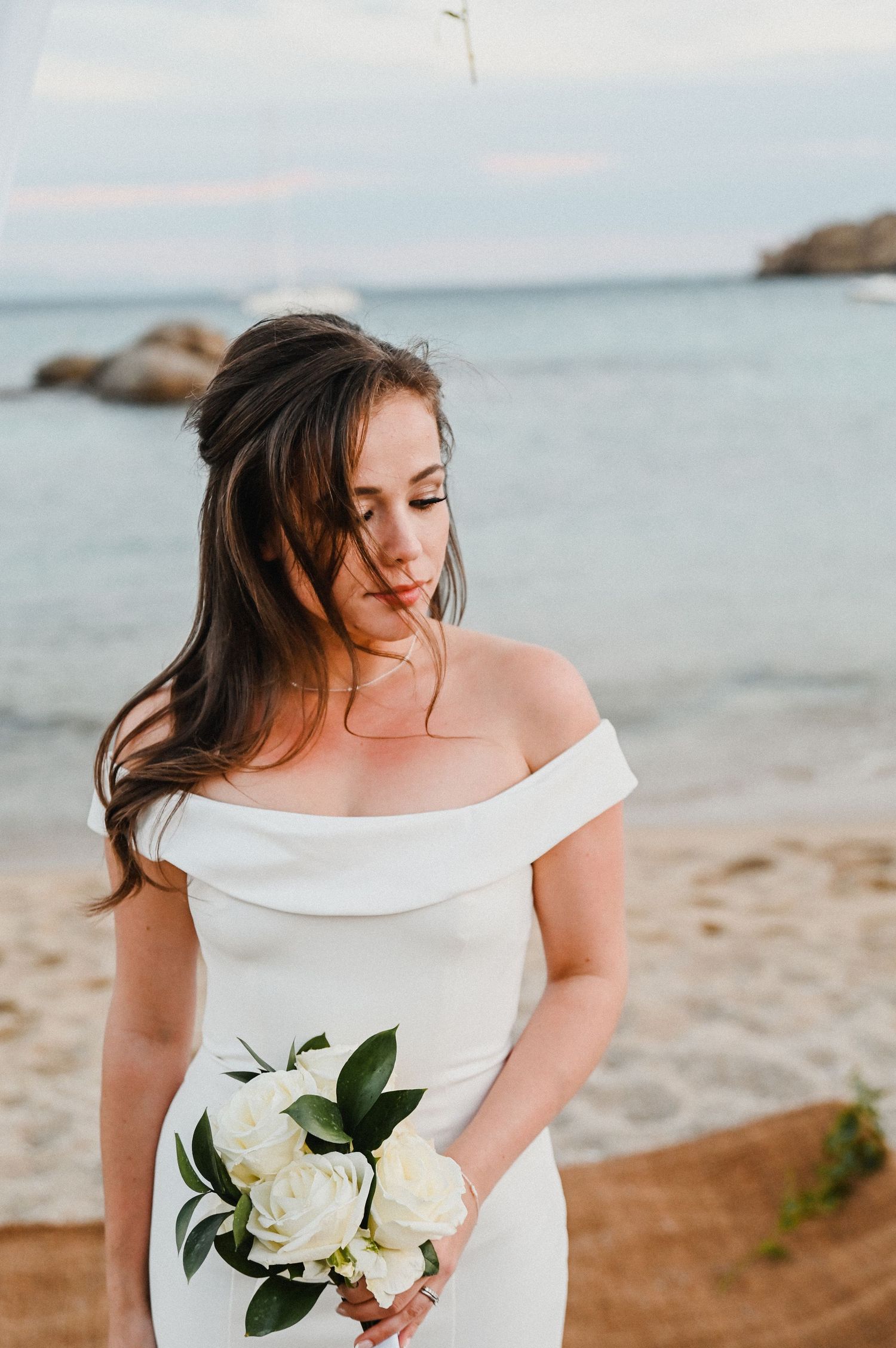 Intimate beach wedding photo with ocean and rocky coastline in the background.
