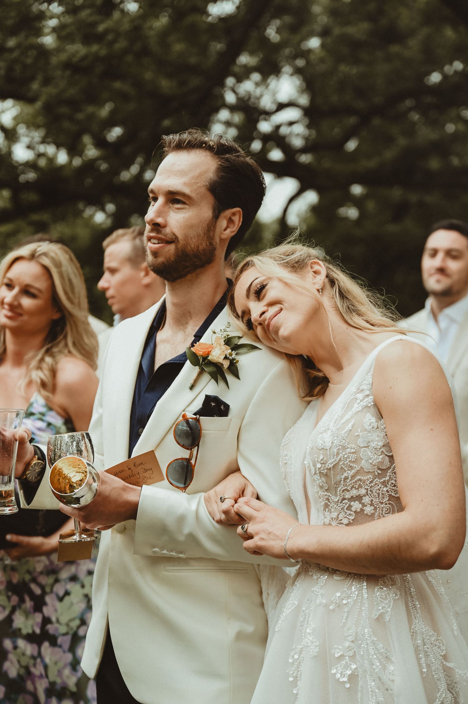 Wedding couple shares a tender moment while holding wine glasses at outdoor reception.
