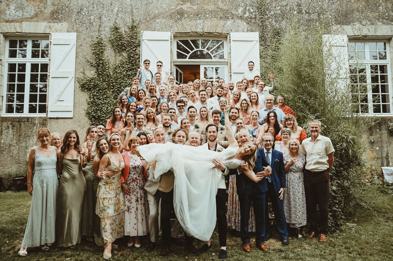 Large wedding group photo on stone building steps with classic architectural details.