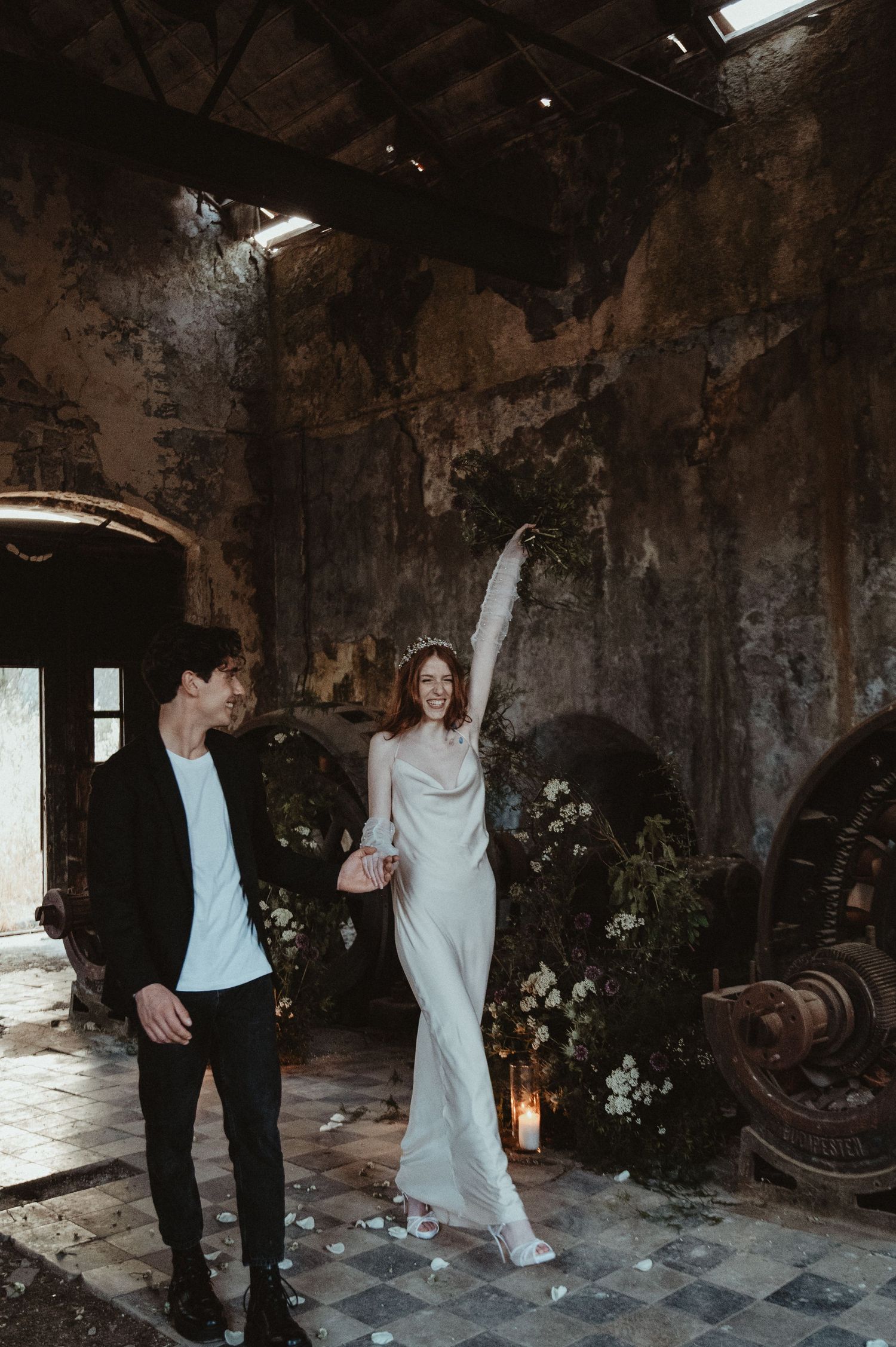 A couple poses in a moody industrial setting with vintage decor and romantic lighting.